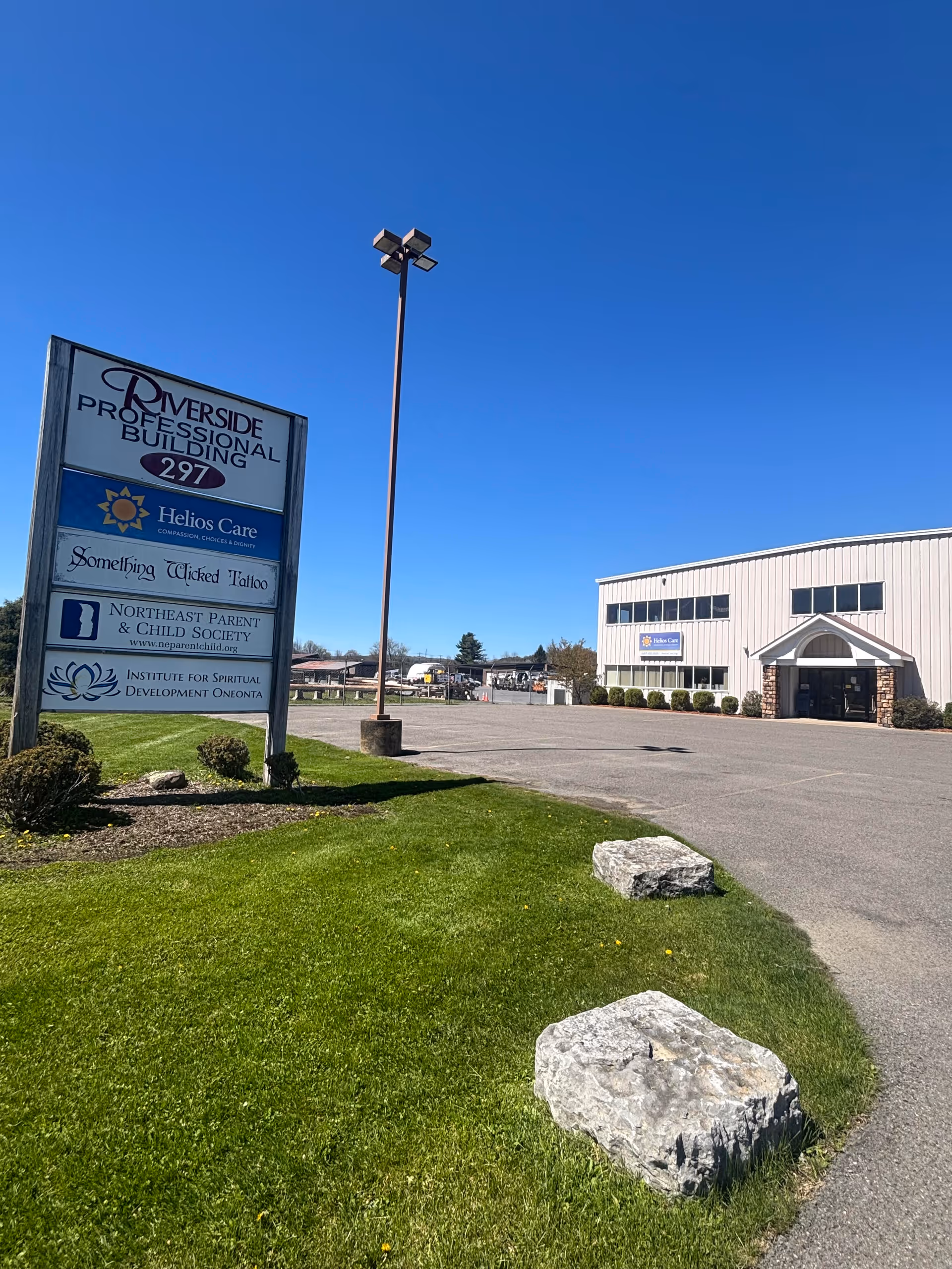 Exterior view of Helios Care facility with sign, lawn, and parking area in front.