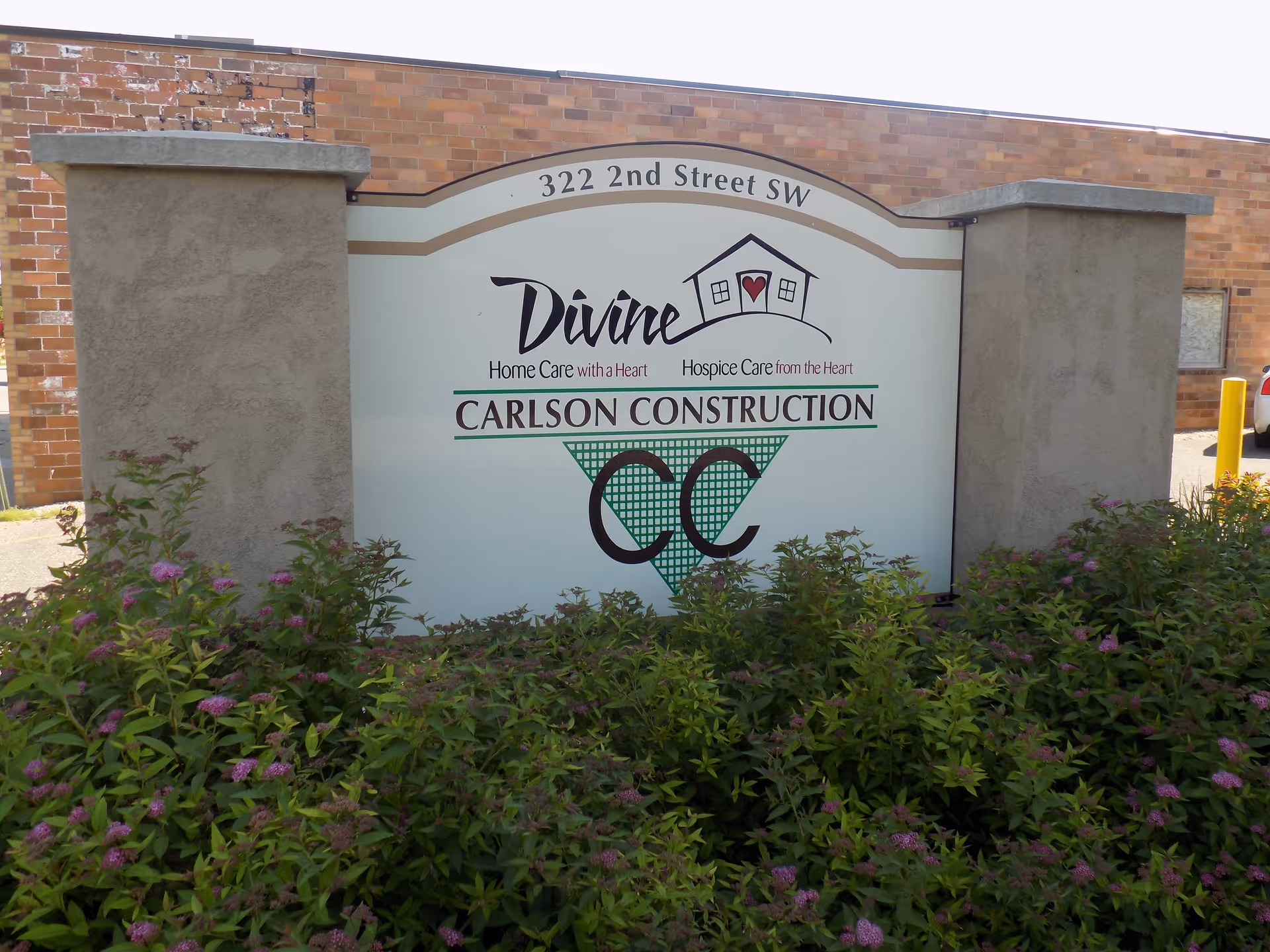 Exterior sign for Divine Home Care and Hospice at 322 2nd Street SW with shrubs.