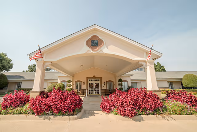 Exterior view of Brookdale Stonebridge Ranch entrance with red flowering bushes and flags.
