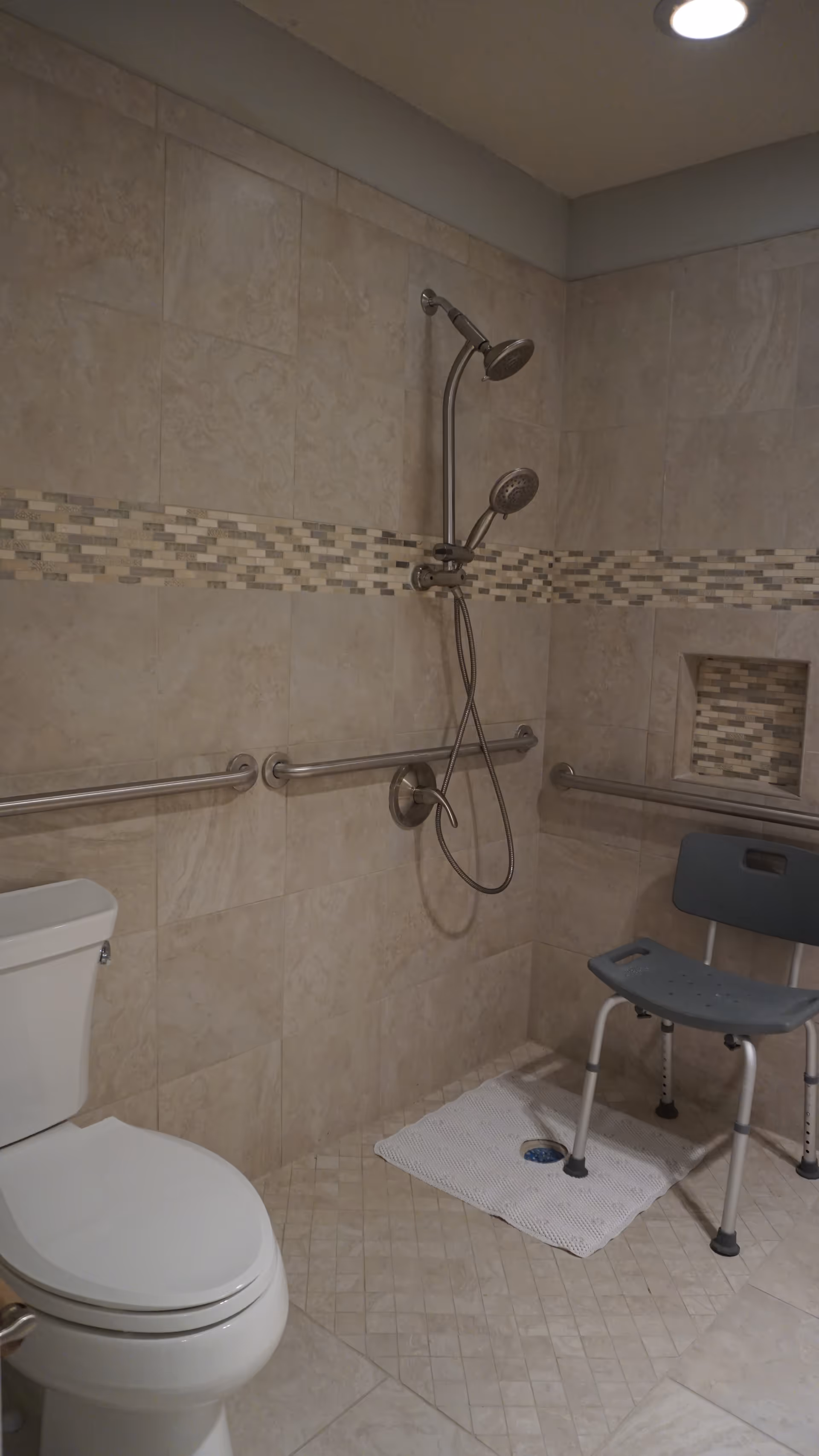 Accessible bathroom with walk-in shower, grab bars, toilet, and a shower chair.