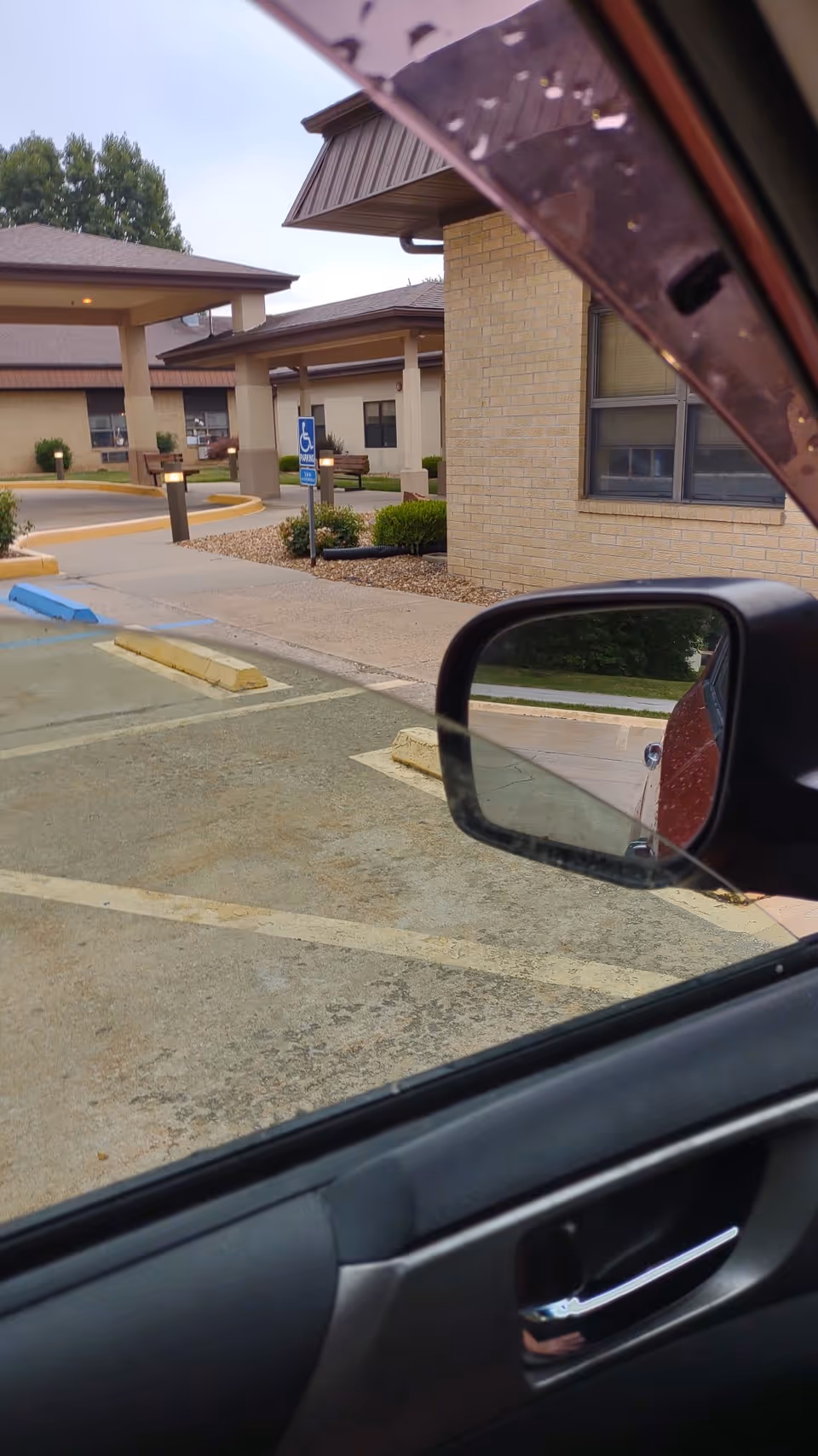 Parking lot view with the facility's brick exterior and car window in foreground.