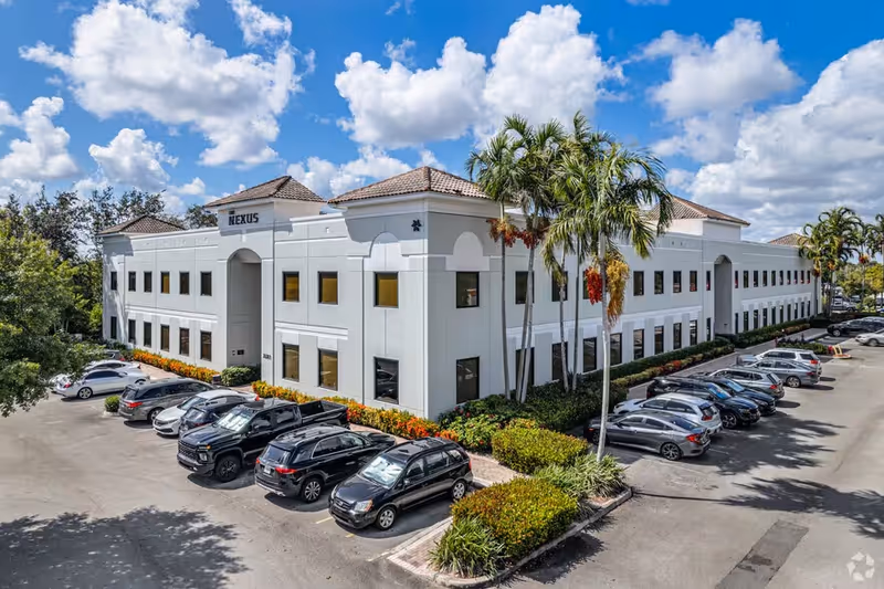 White two-story building with palm trees and a parking lot