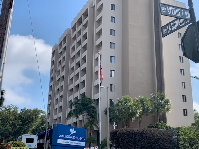 Tall beige senior living building with blue entrance sign reading Lake Howard Heights, palm trees
