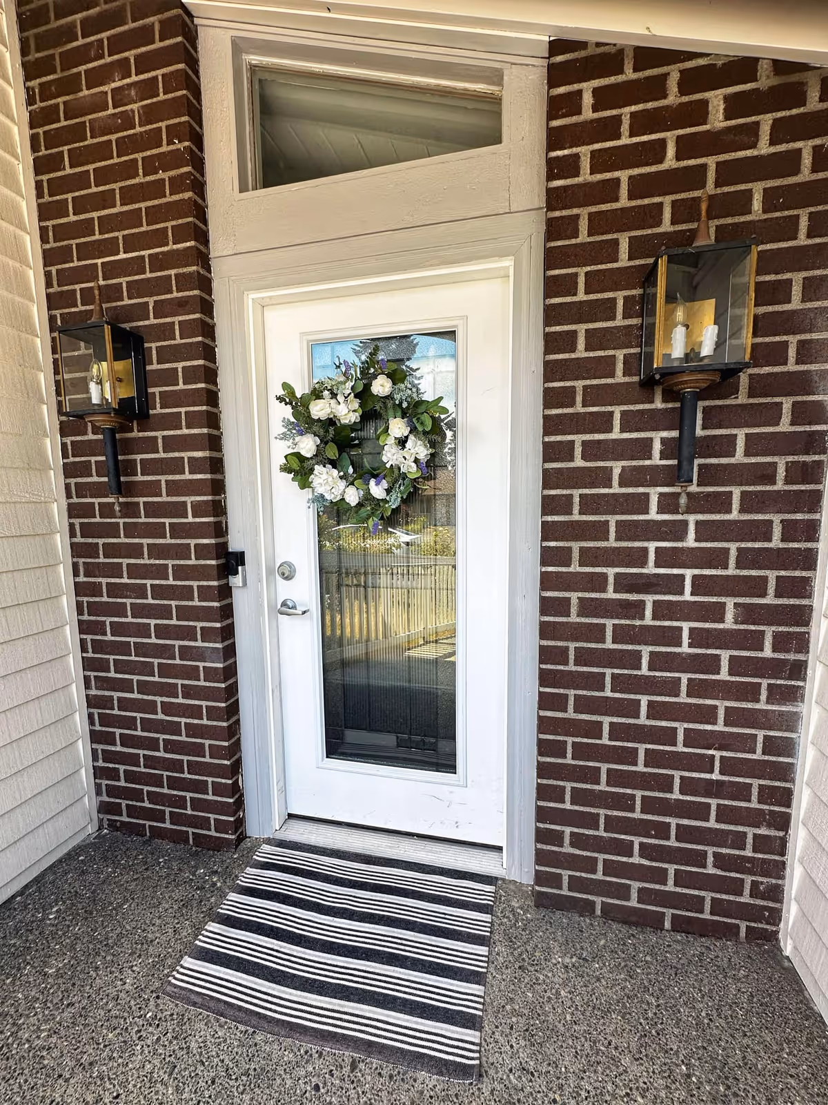 White front door with wreath, brick exterior, striped welcome mat.