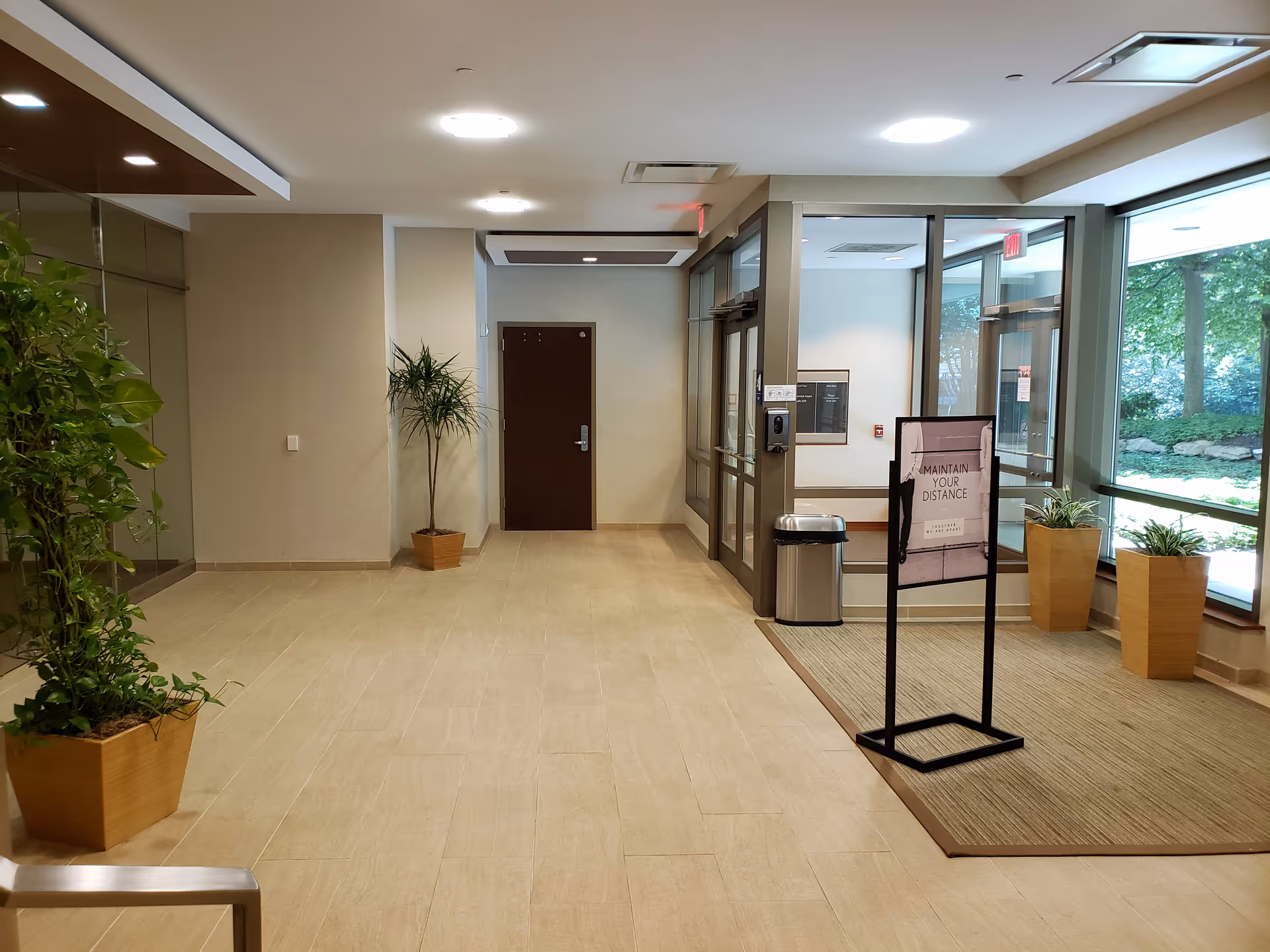 Interior lobby of a senior living facility with glass doors, potted plants, and signage.
