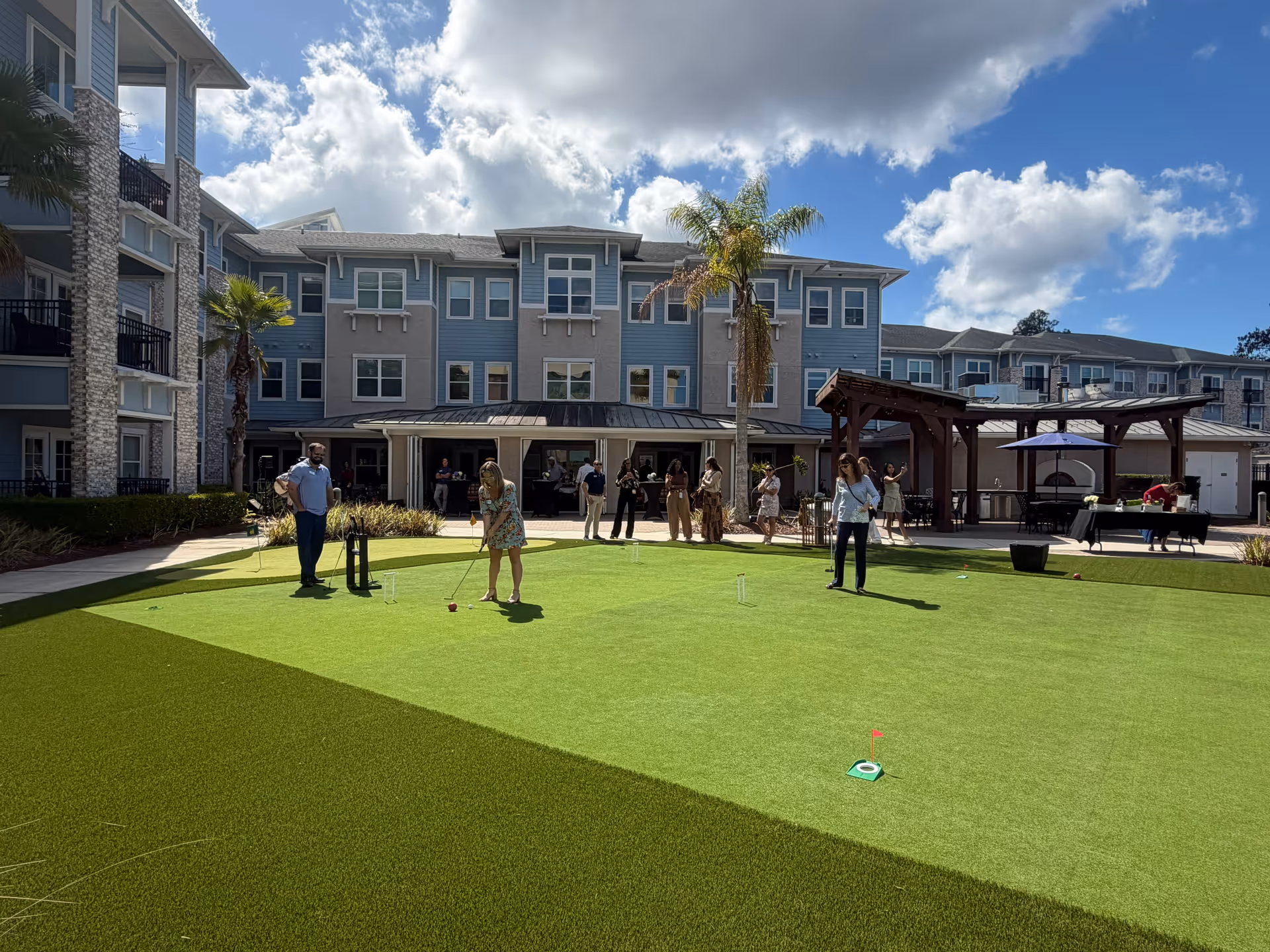 Residents and staff play mini-golf on a sunny outdoor courtyard.