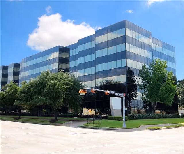 Modern glass building with trees and blue sky in the foreground