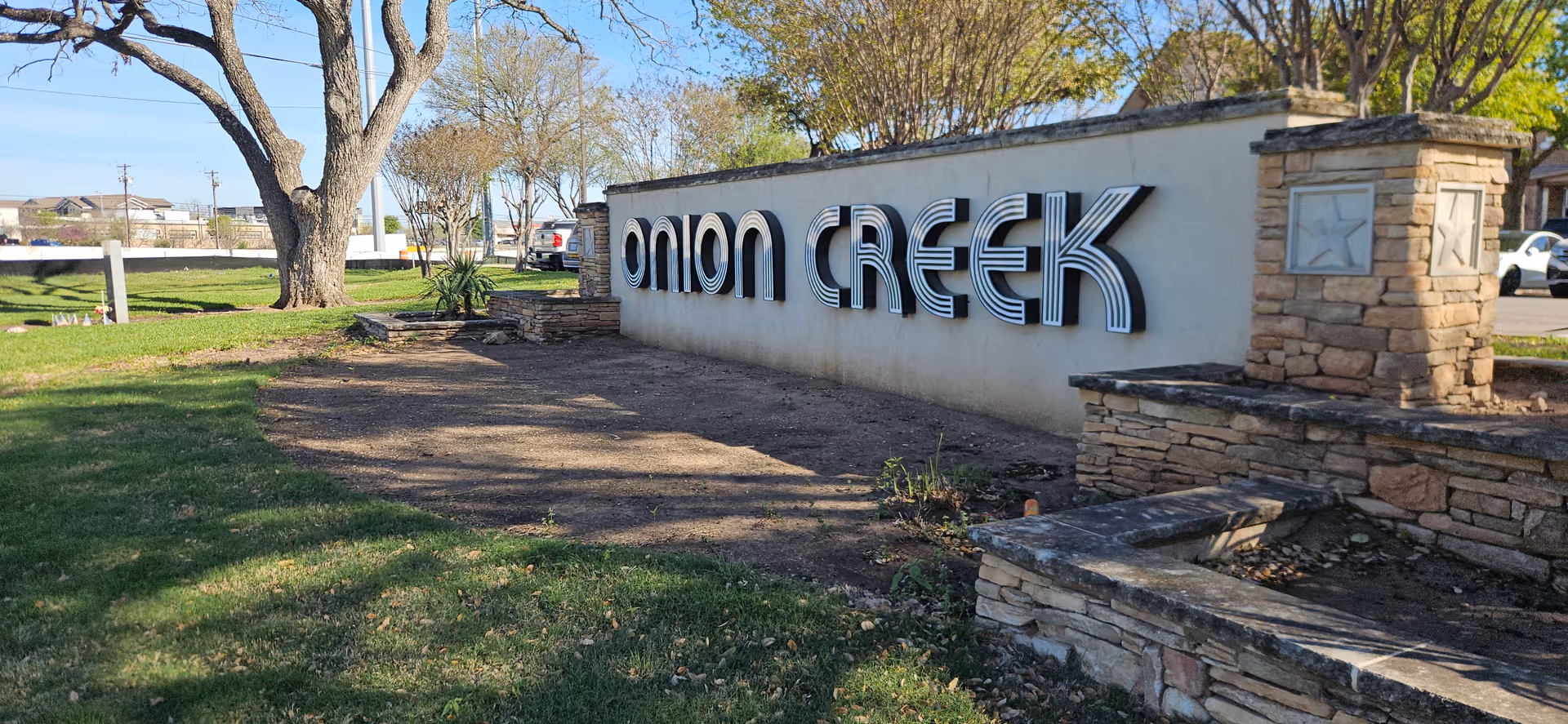 Outdoor entrance sign reading Onion Creek on a white wall with trees and landscaping.