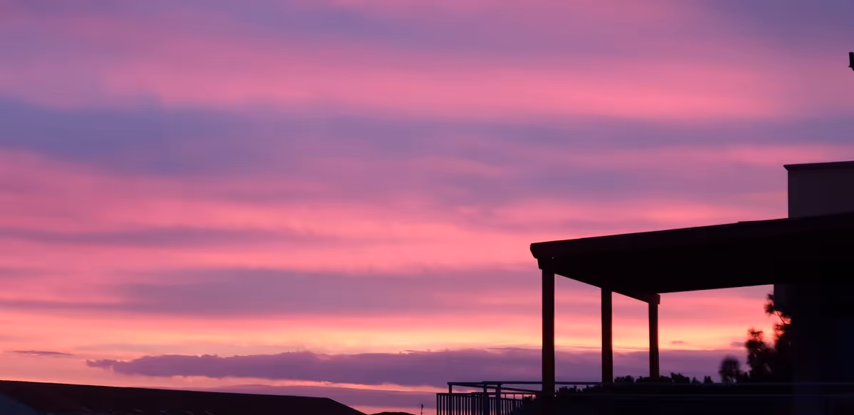 Sunset sky behind a silhouetted building with a covered outdoor balcony.