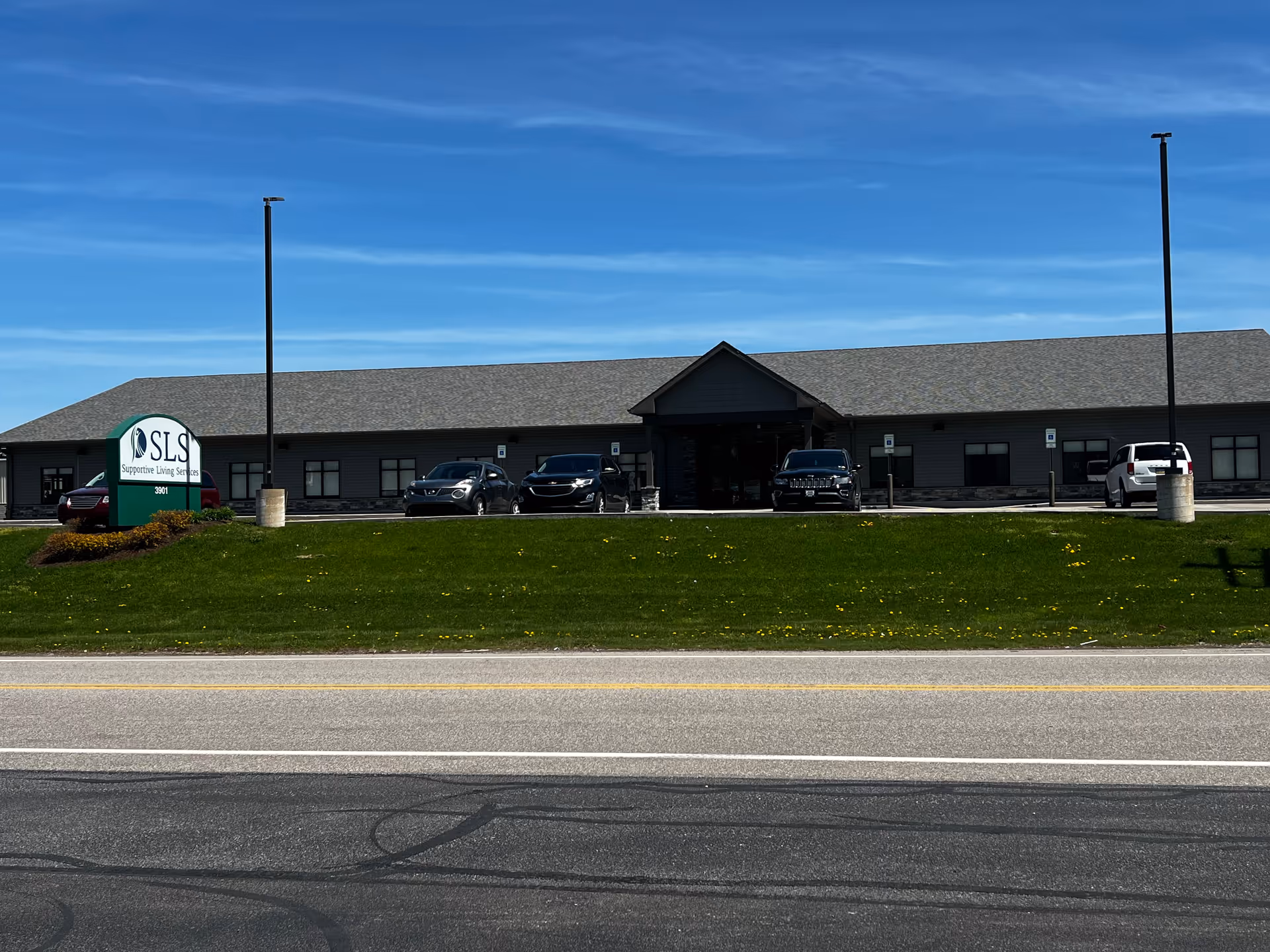 Exterior of Supportive Living Services Inc building with parked cars and green lawn.