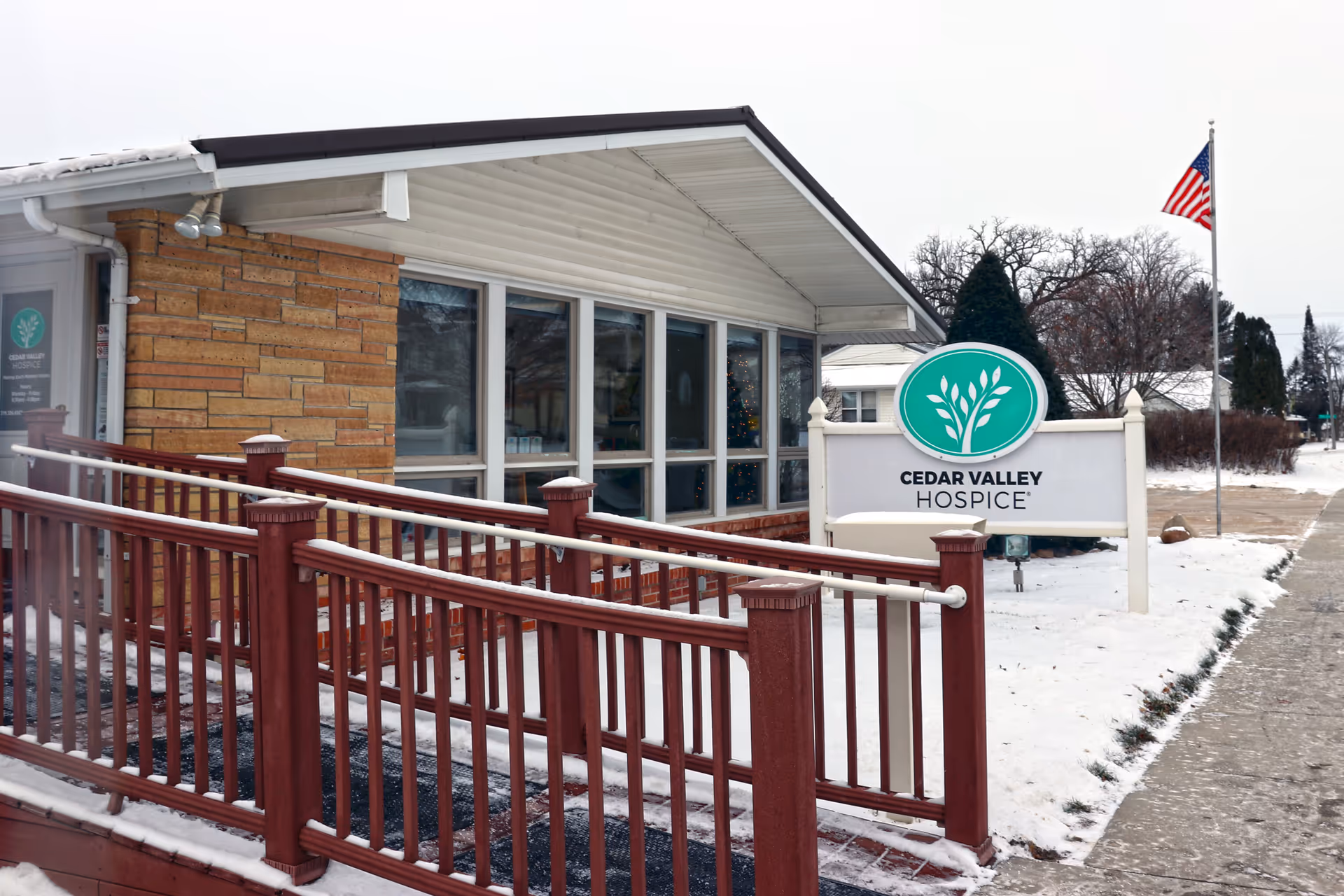 Exterior view of Cedar Valley Hospice building with a front sign, snow, and flag.