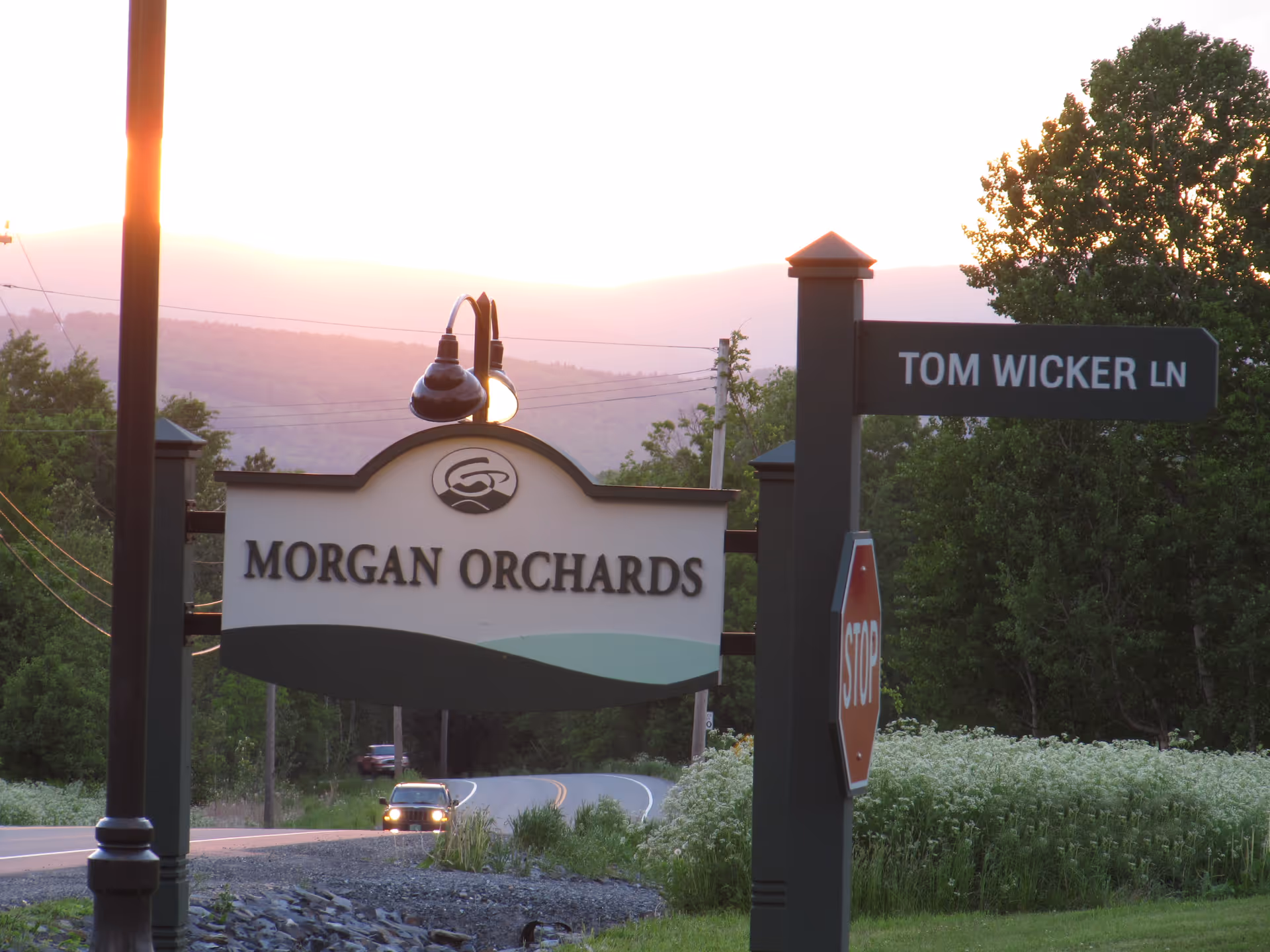 Sunset outdoor scene with Morgan Orchards sign and Tom Wicker Ln street sign.