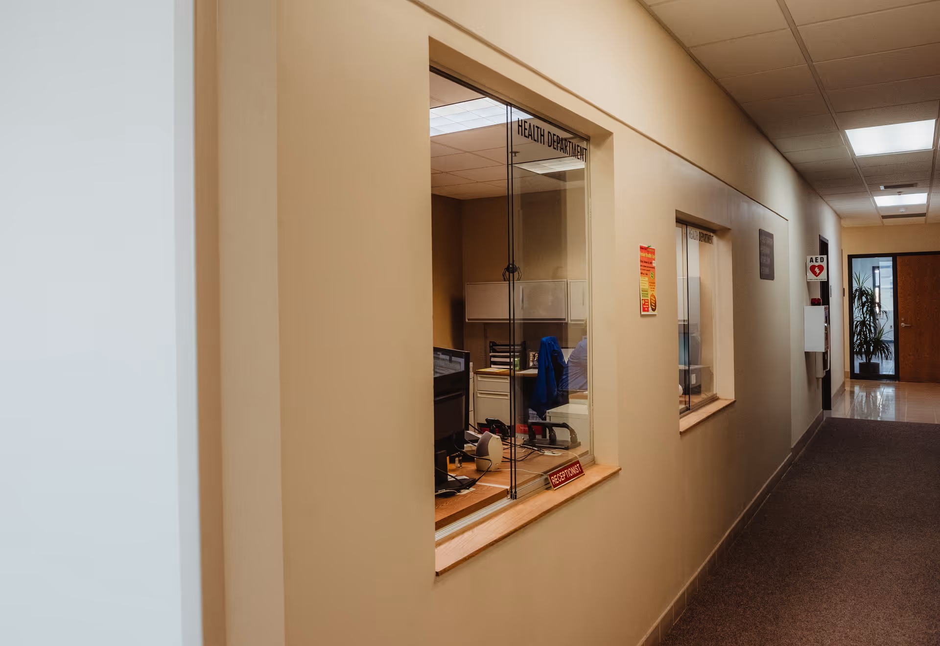 Beige interior hallway with a reception window and health department offices.