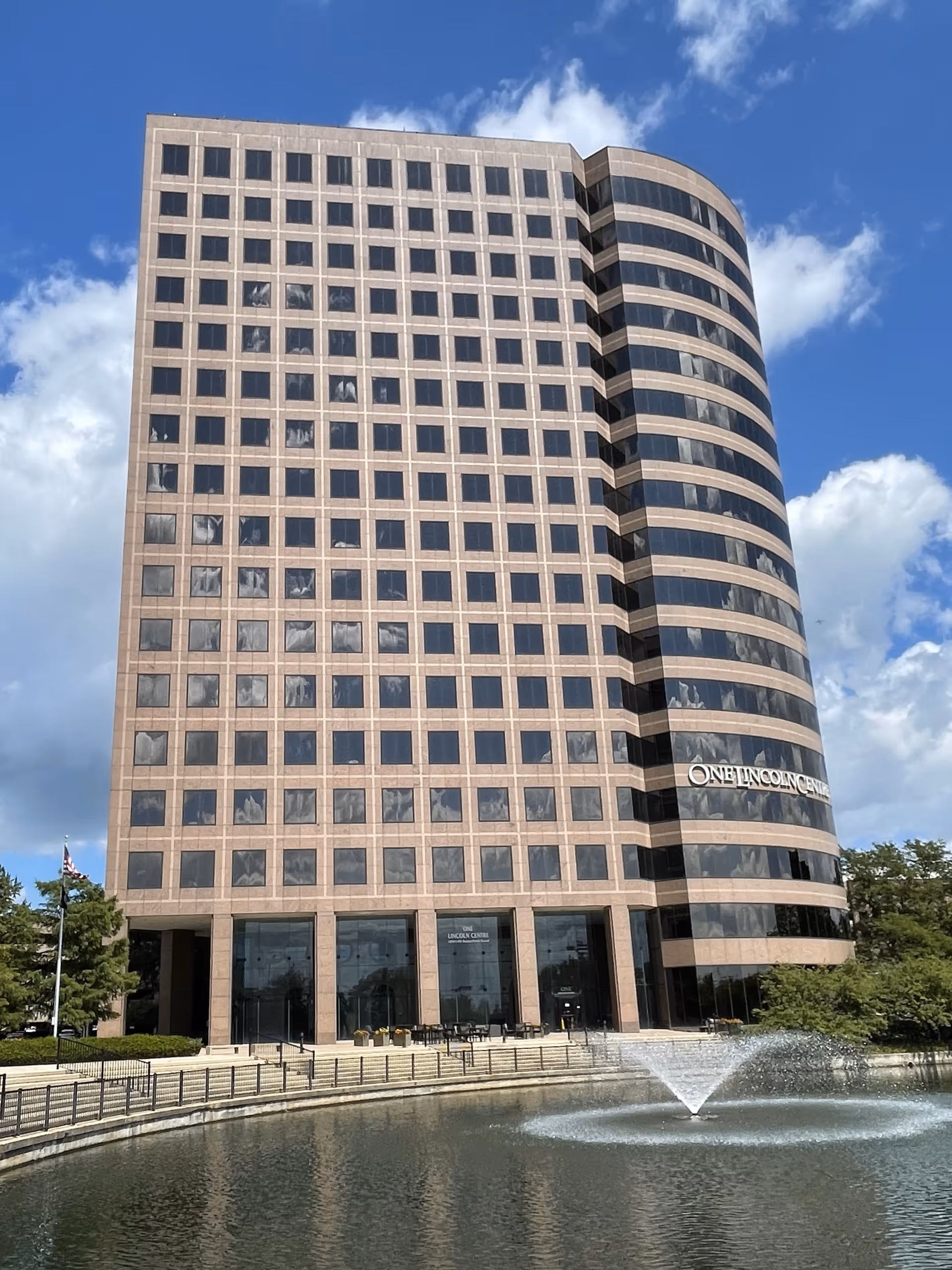 Tall modern building with curved glass facade and a fountain plaza in front.
