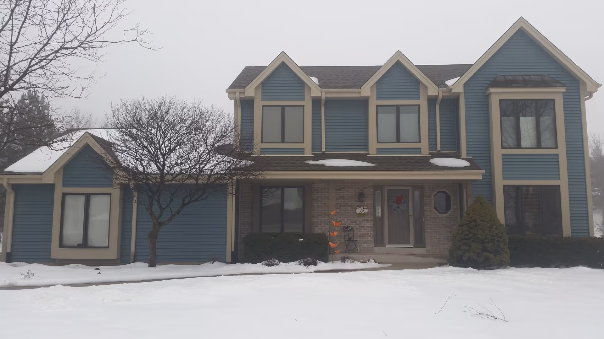 Front exterior of a blue multi-gabled senior living building in snow.