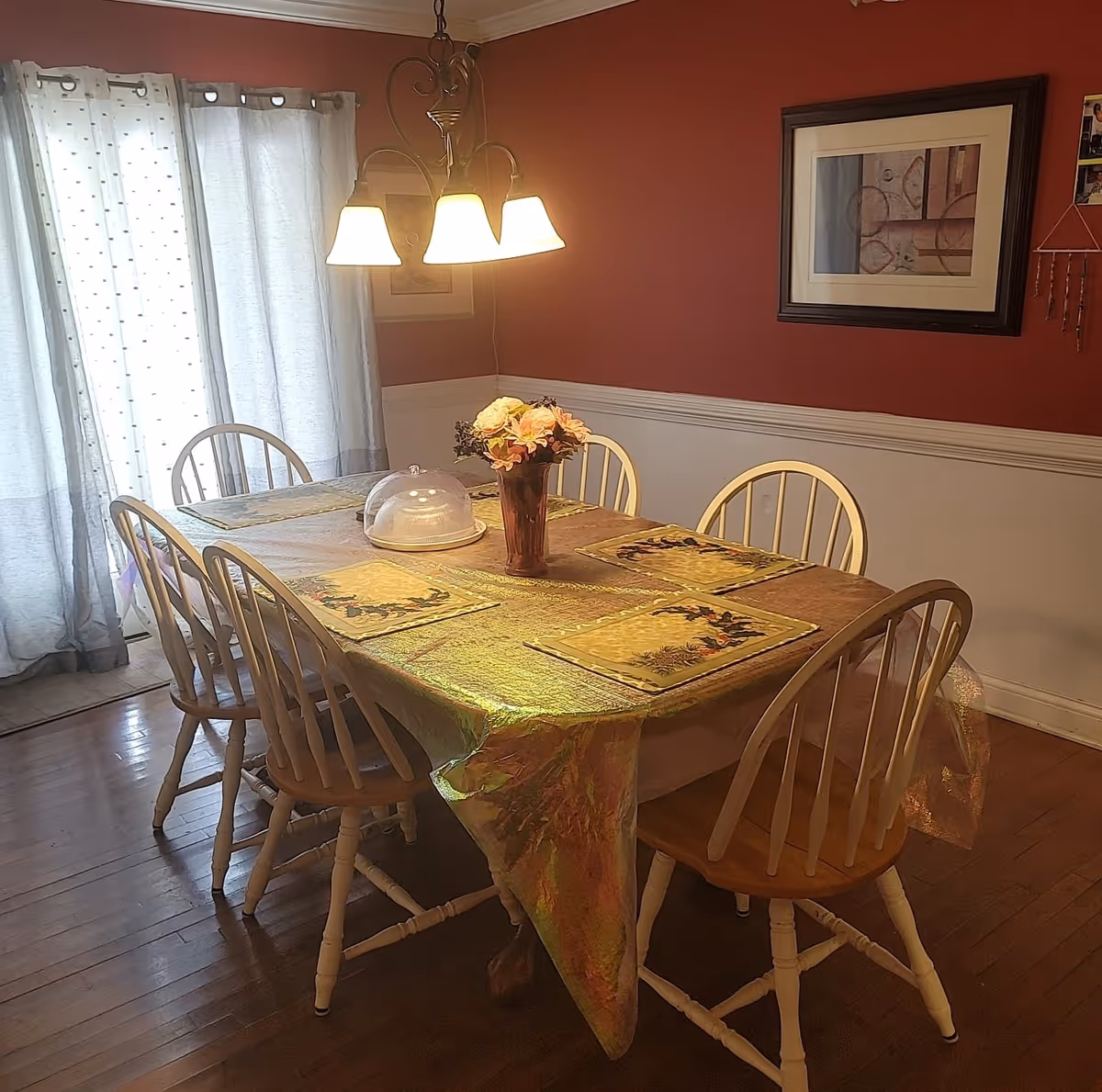 Dining room with wooden table, chairs, flowers, warm lighting, and red wall.