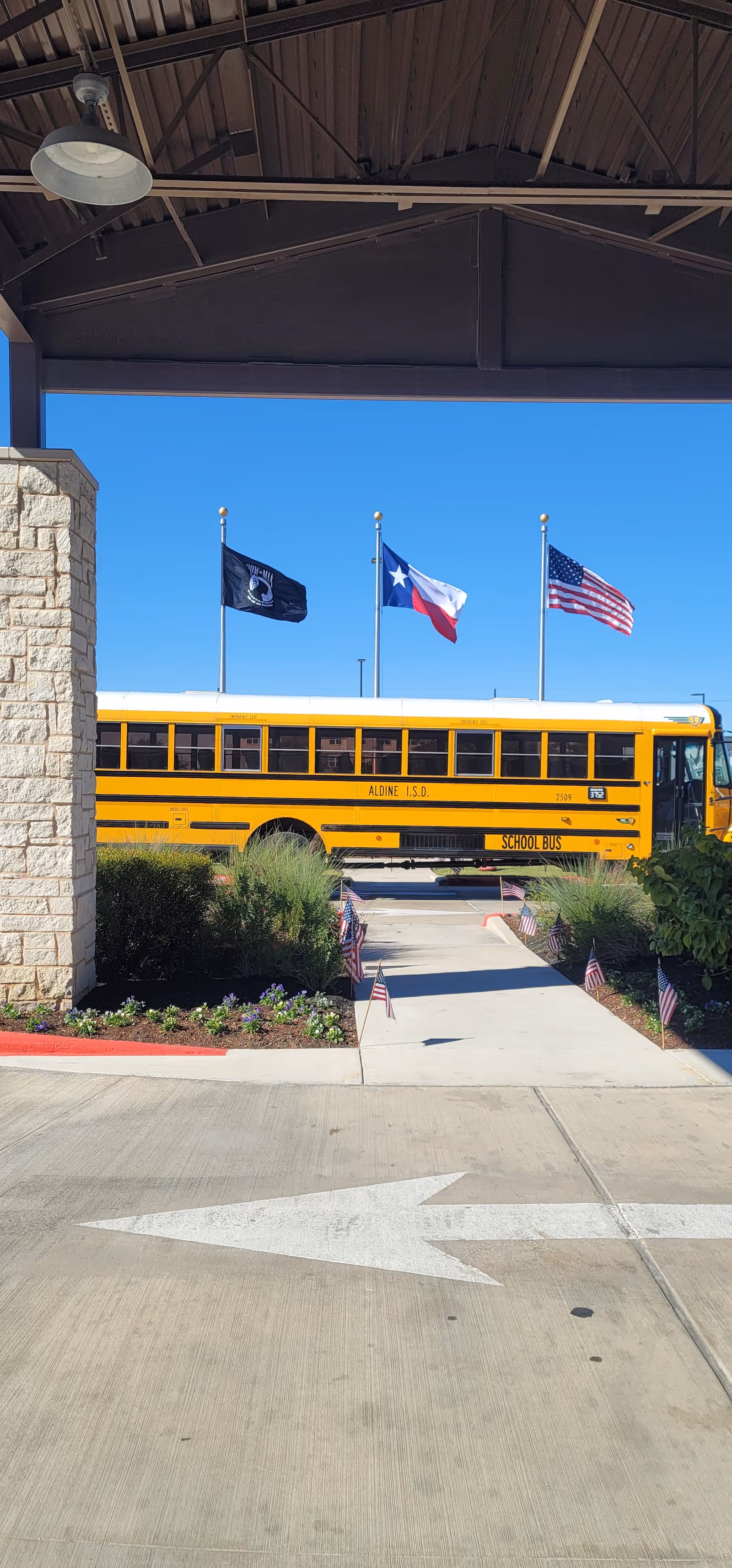 Yellow school bus parked outside a facility entrance under a covered canopy with flags