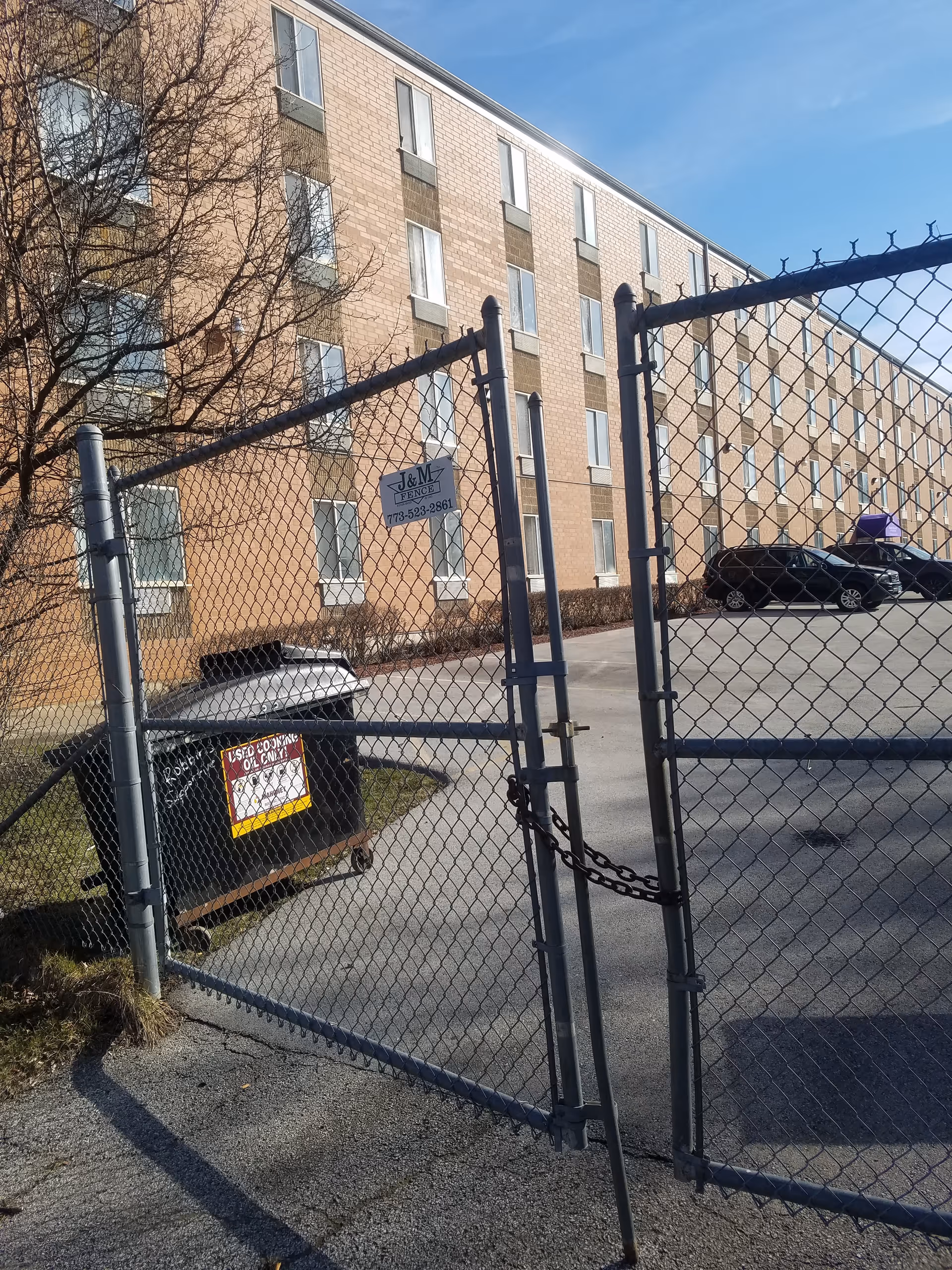 Chain-link gate in front of a brick senior living building with parked cars.