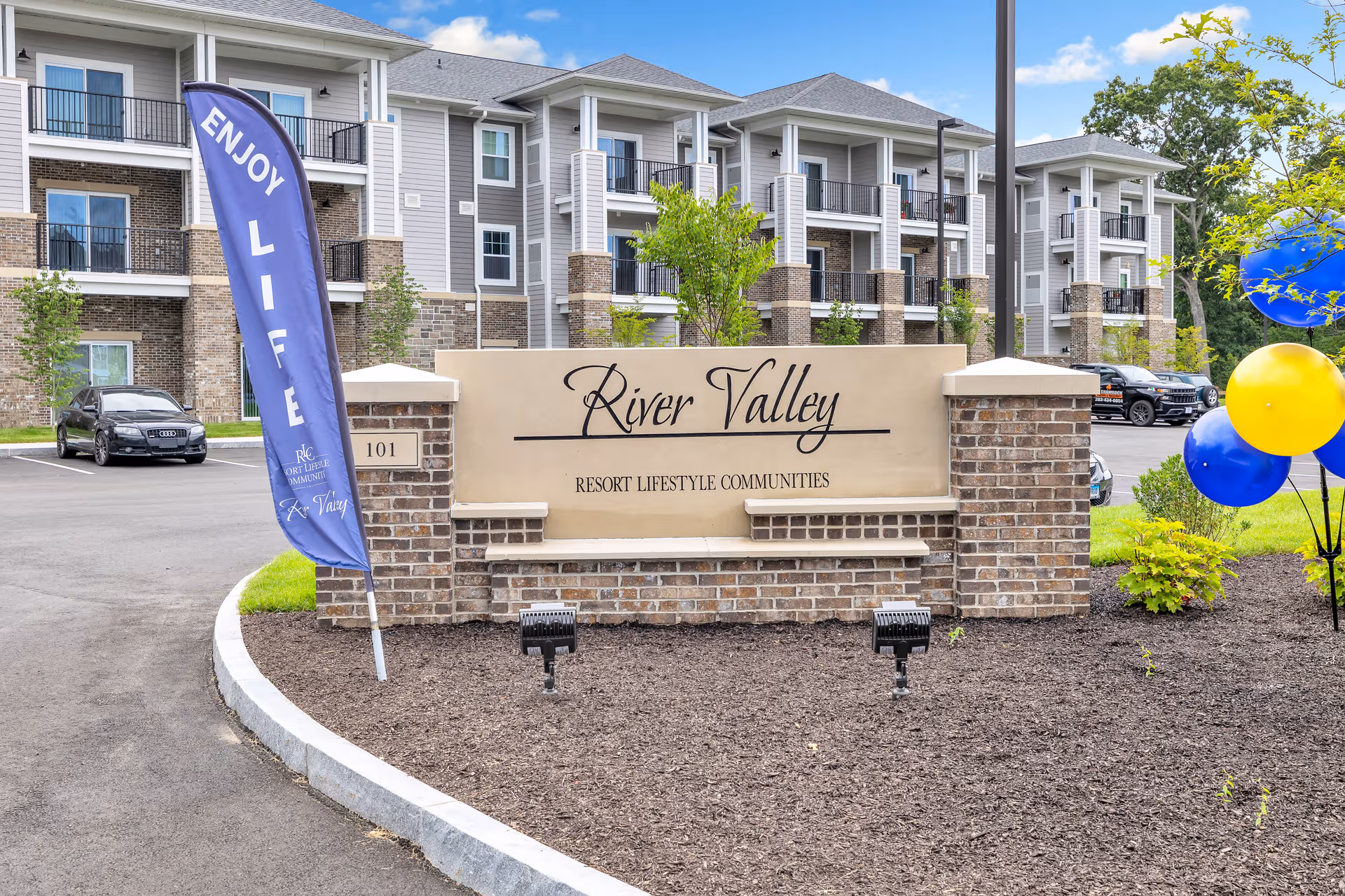Exterior view of River Valley Retirement Community entrance with a brick sign and balloons.