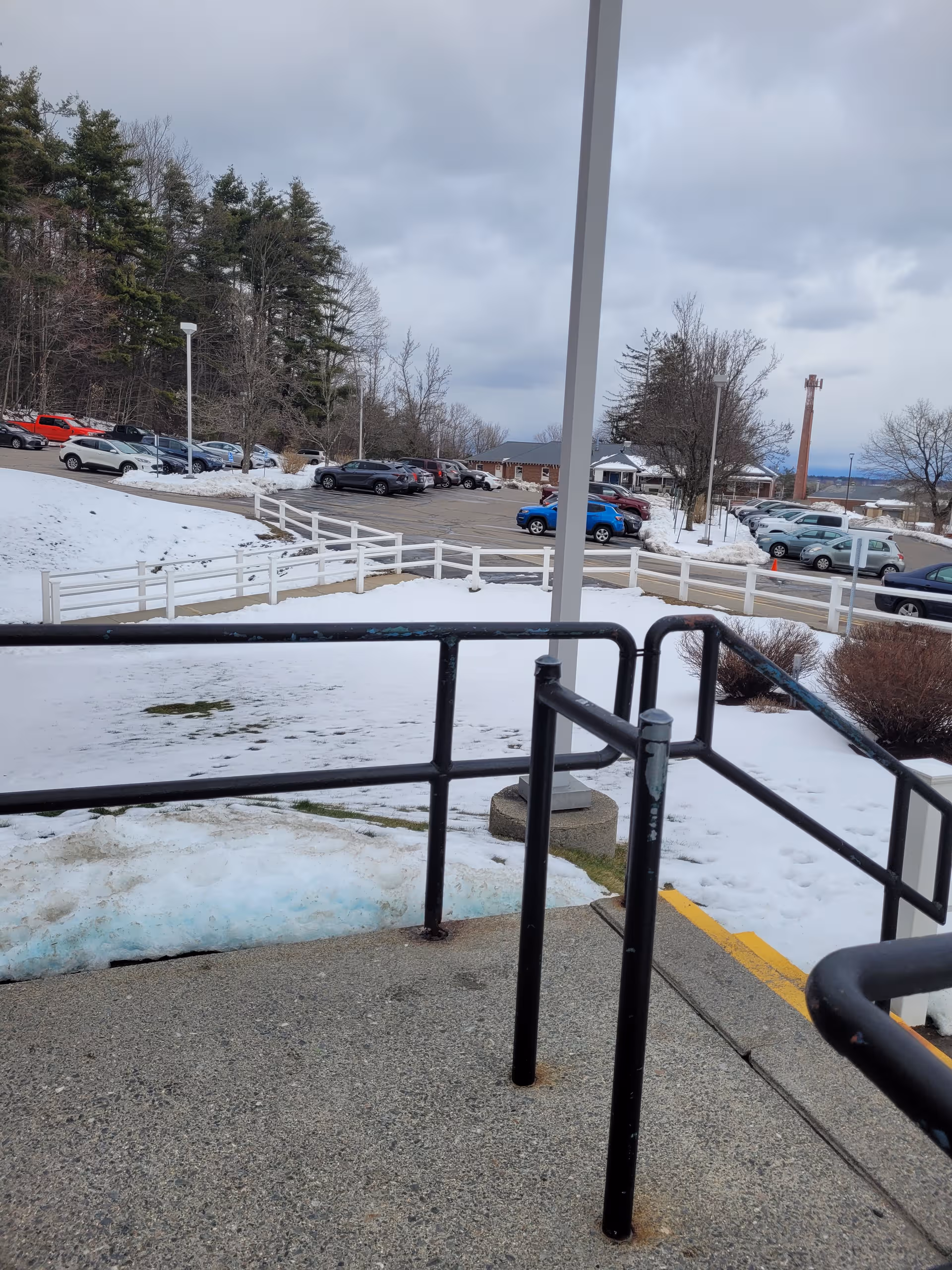 Snowy outdoor view of the facility's parking lot, railing, trees, and overcast sky.