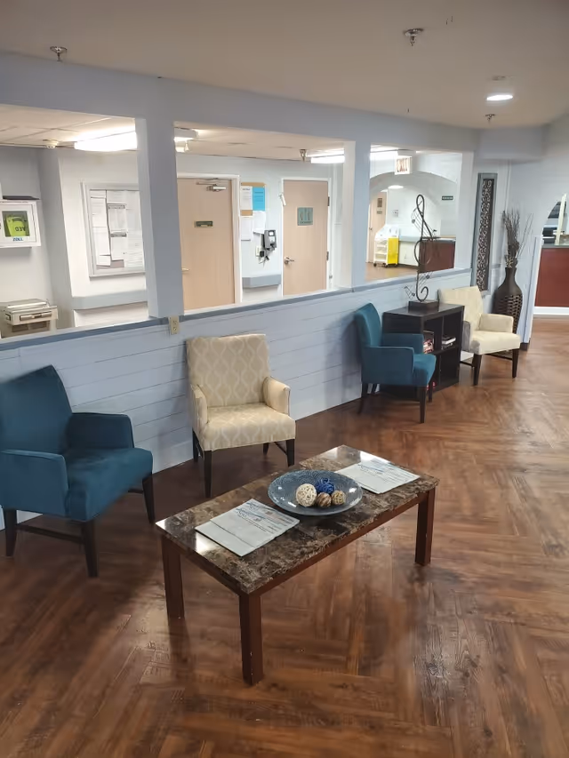 A blue lobby in a senior facility with teal chairs, a marble coffee table, and magazines.