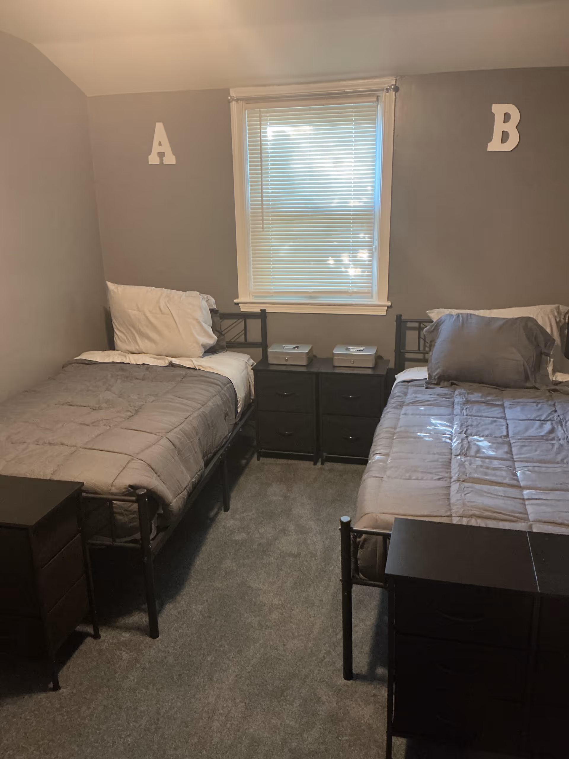 Two twin beds with nightstands flank a window in a small shared bedroom.