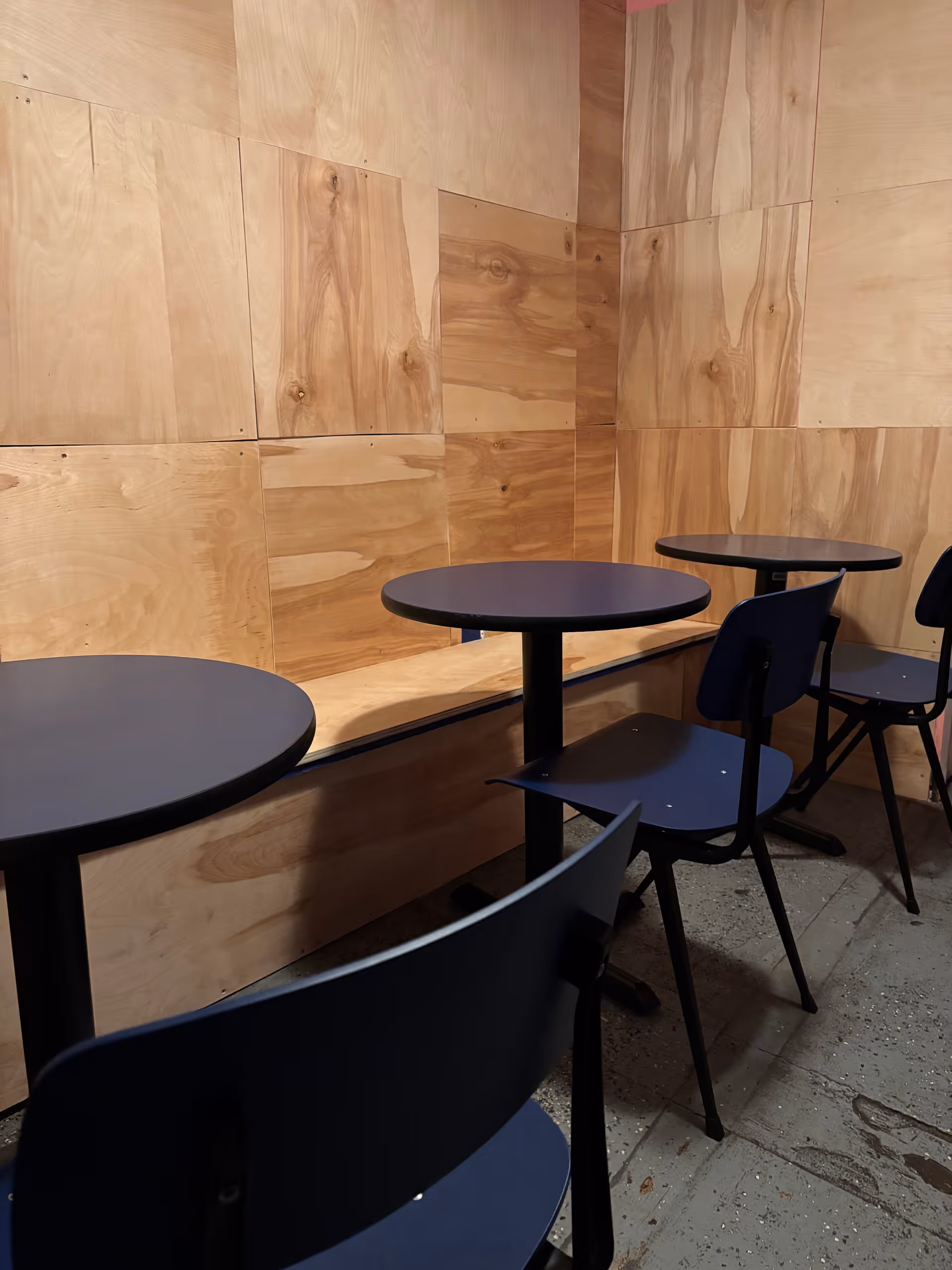 Wood-paneled walls surround round blue tables and chairs in a small dining area.