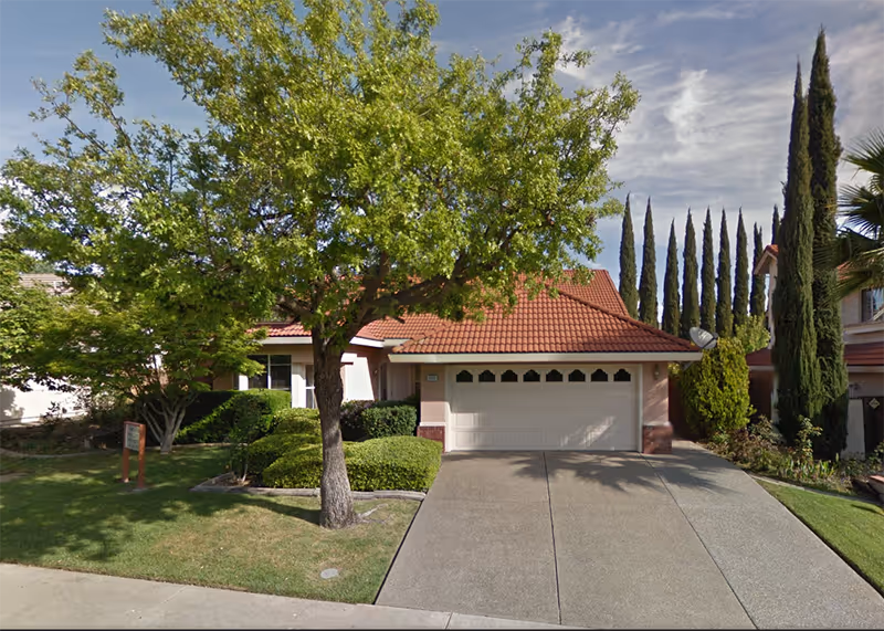 Front exterior of Tuscany Villa Care Home with a driveway, trees, and a two-car garage.