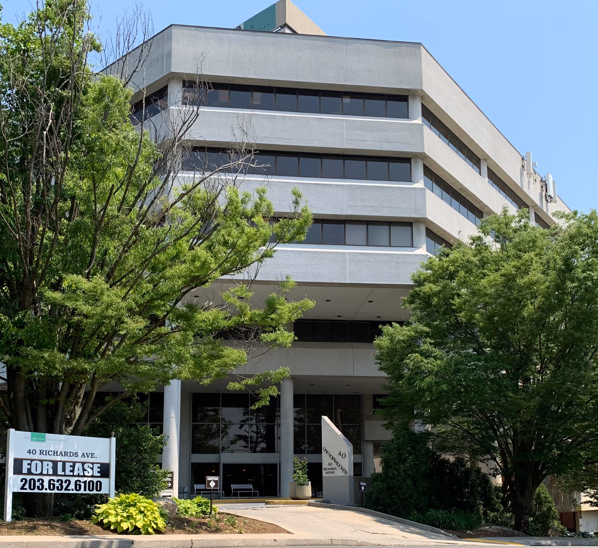 Exterior view of a multi-story building with surrounding green trees and a 'For Lease' sign.