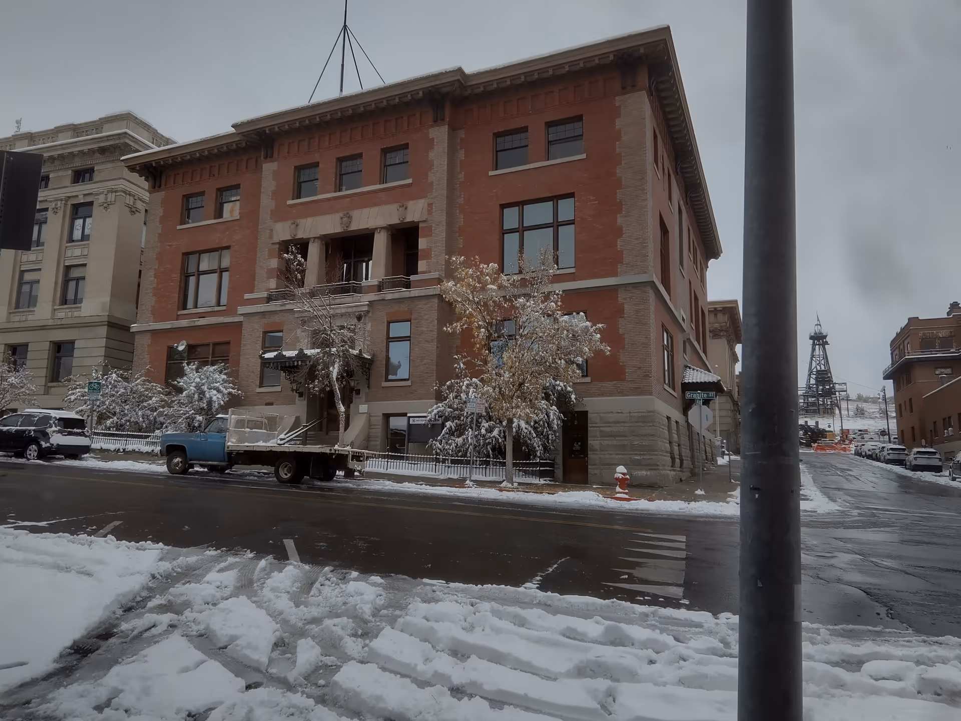 Snow-covered brick building on a city street with parked vehicles.