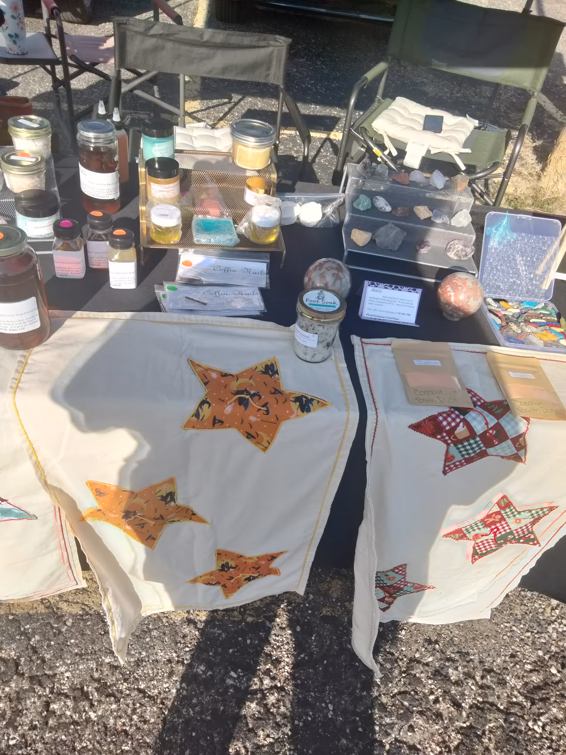 Outdoor market display with jars, rocks, candles, and patchwork quilts on tables.