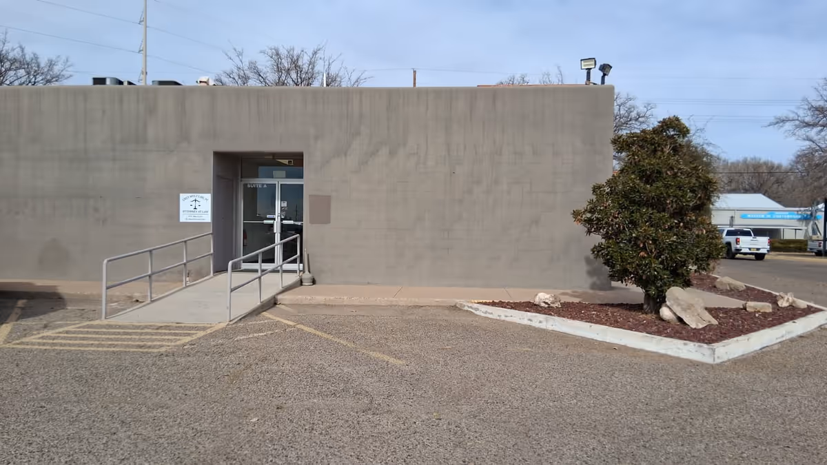 Front exterior of a beige facility with ramp, landscaping, and entrance door.