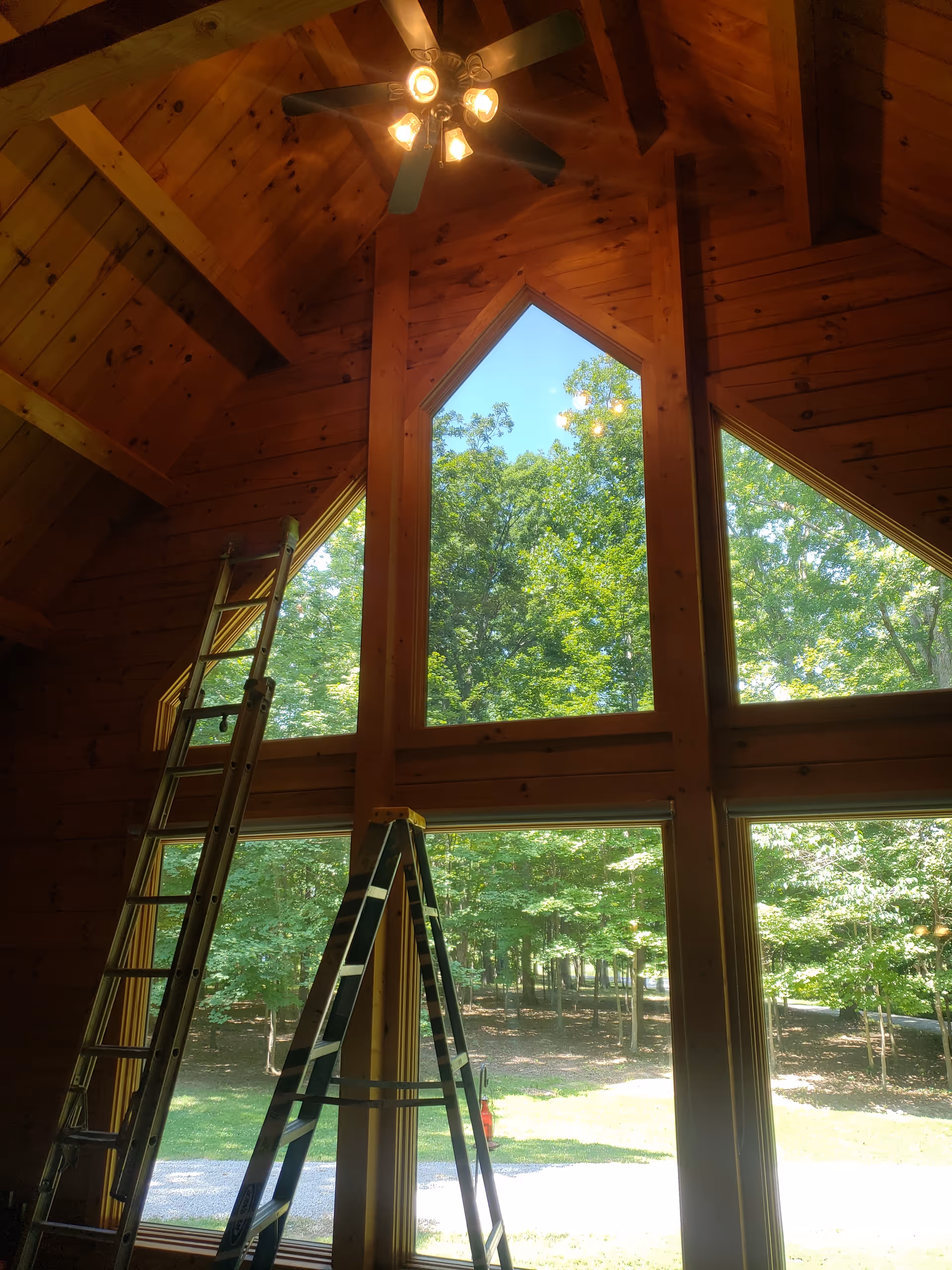 A wooden vaulted interior with large triangular windows, ladders, and a ceiling fan.