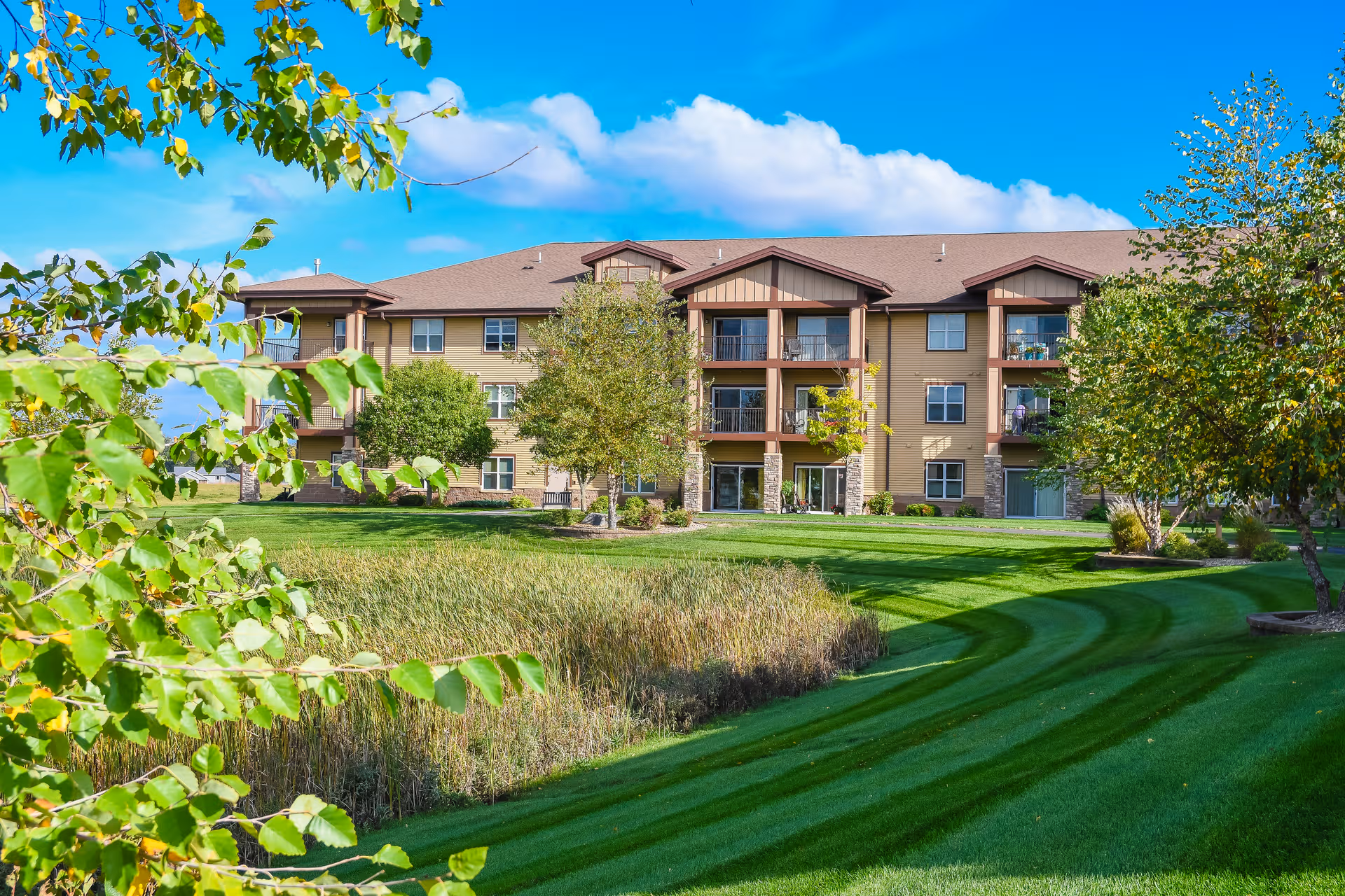 A multi-story senior living building with balconies, set among manicured lawns and trees.