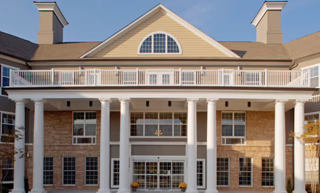 Front view of a brick senior living facility with tall white columns and a balcony.