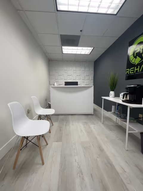 Reception area inside a clinic with white chairs, a white front desk, and a coffee station.