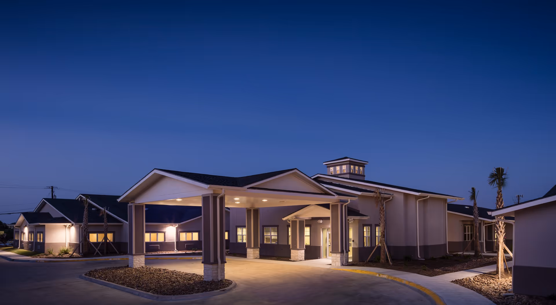Memory care center exterior at dusk with lit entrance and circular driveway.