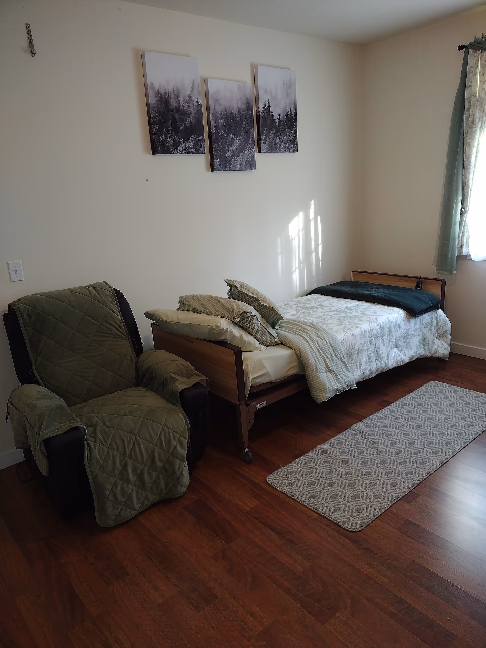 Small bedroom with a single bed, a green-covered recliner, wall art above the bed, and a patterned runner on a wooden floor.