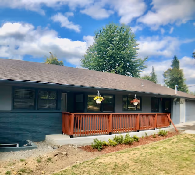 Single-story senior care facility exterior with a brown railing and hanging flower baskets.