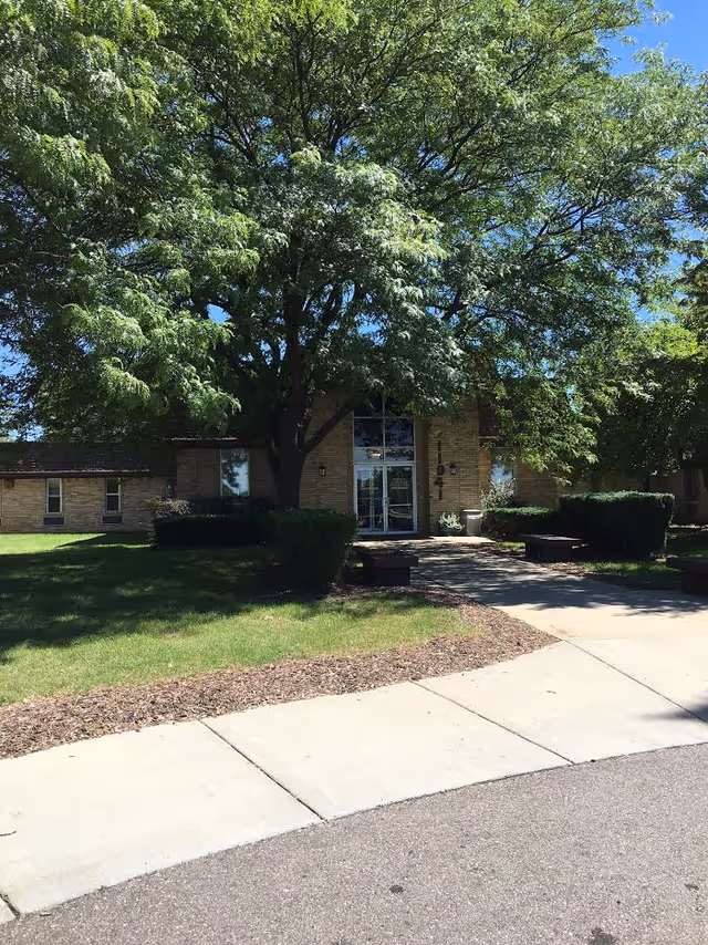 Front entrance of Medilodge of Grand Blanc with a large tree and green landscaping.