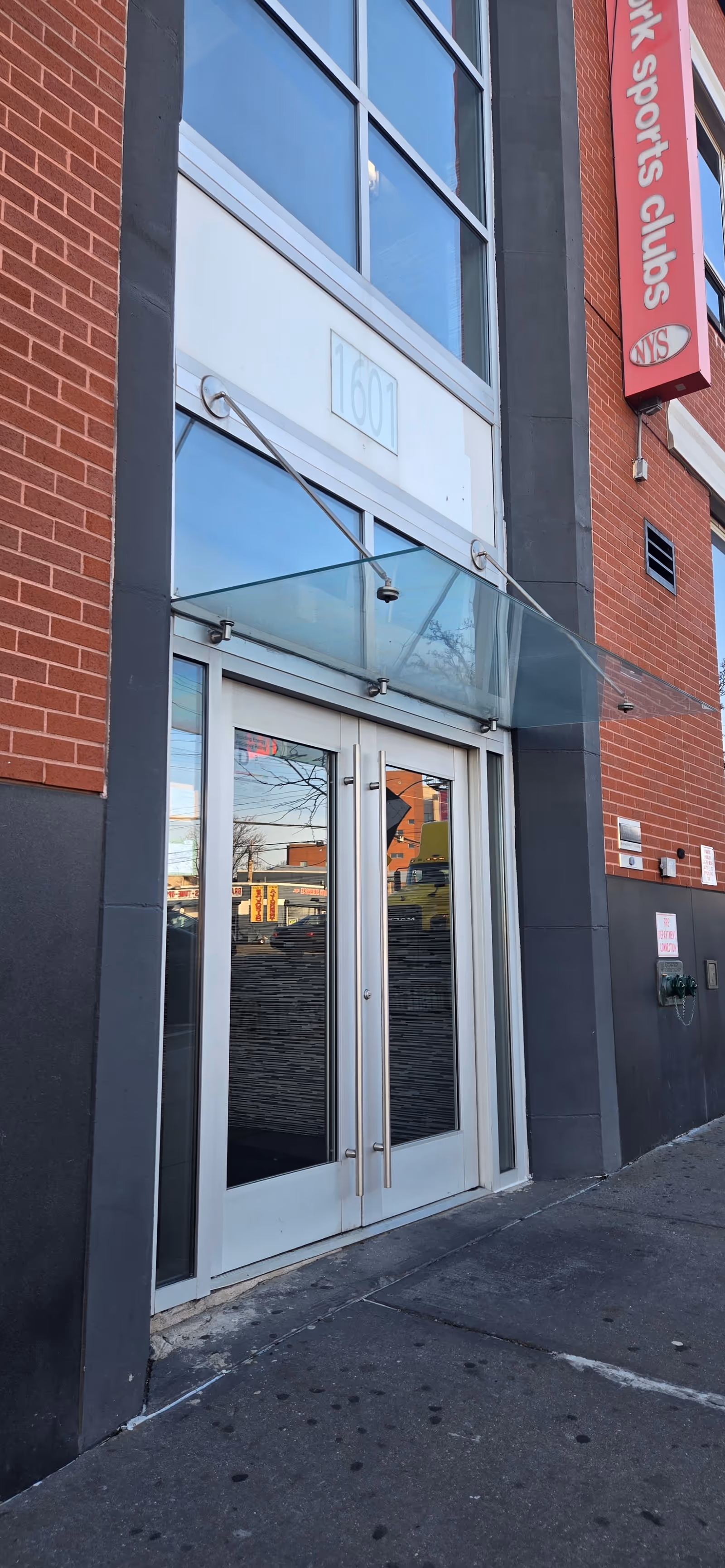 Exterior brick building entrance with glass double doors and a glass canopy.