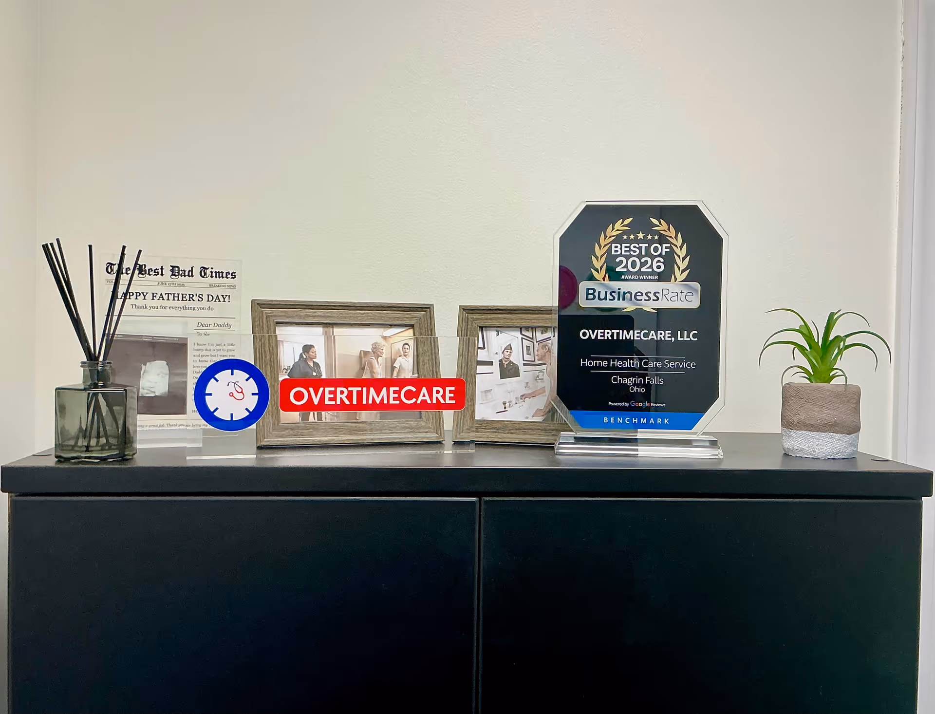 A black cabinet displays awards, photos, a plant, and a red OvertimeCare sign on top.