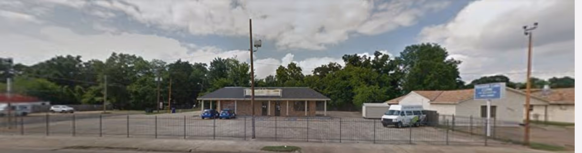 Exterior view of a senior living facility front, fenced lot, with parked vans.