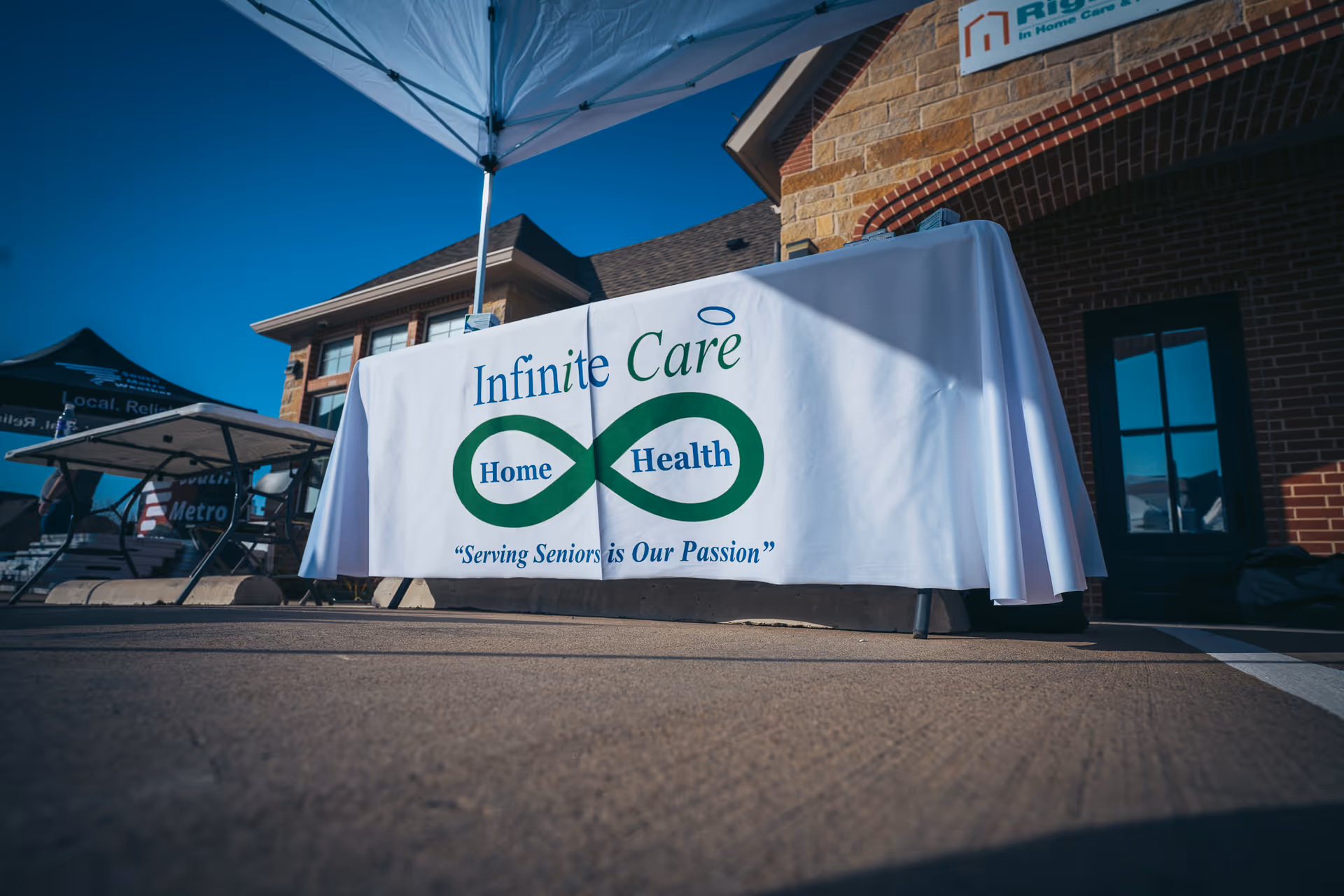 Outdoor scene with an Infinite Care Home Health banner on a table beside a brick building