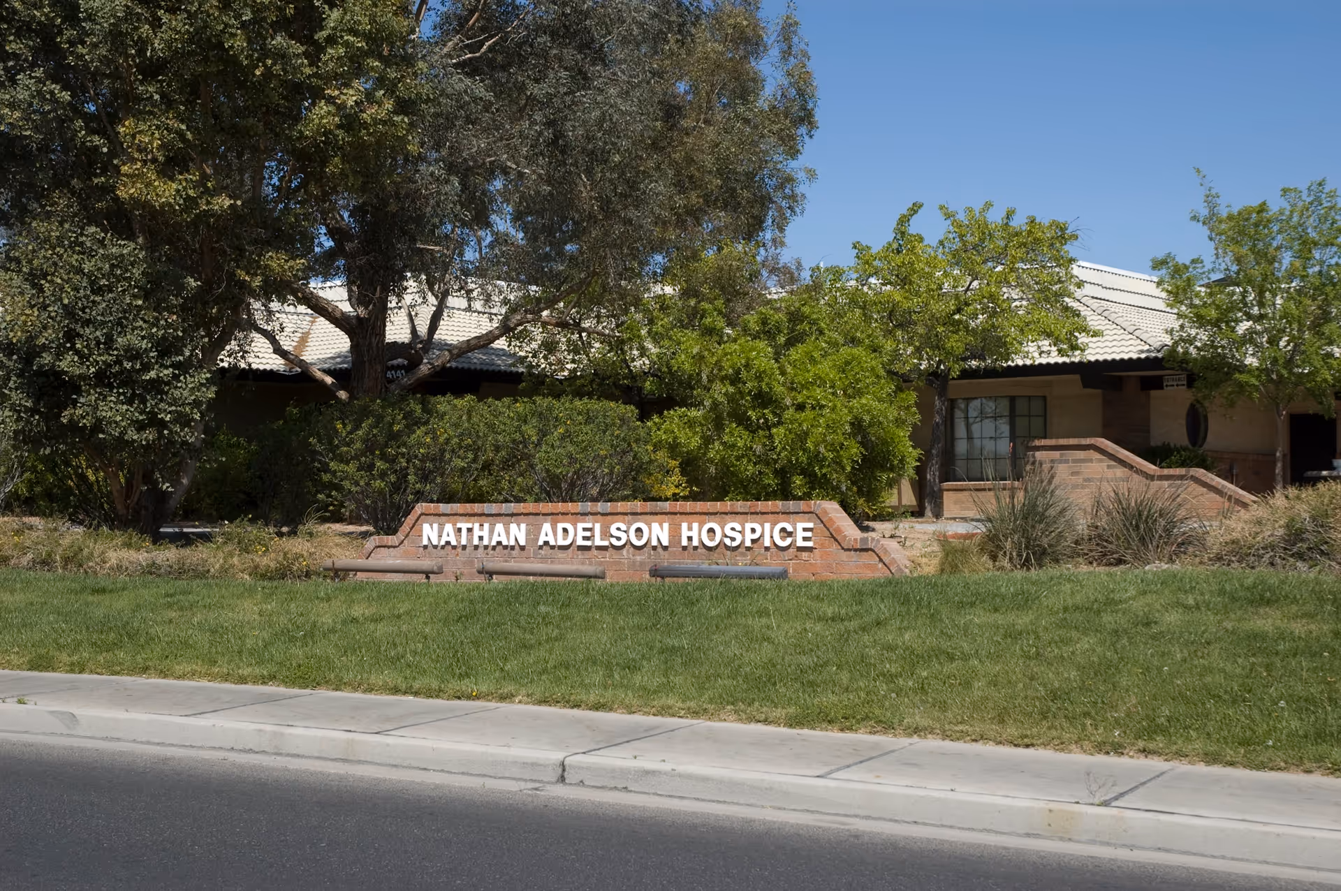 Exterior view of Nathan Adelson Hospice with a brick sign and manicured landscaping.