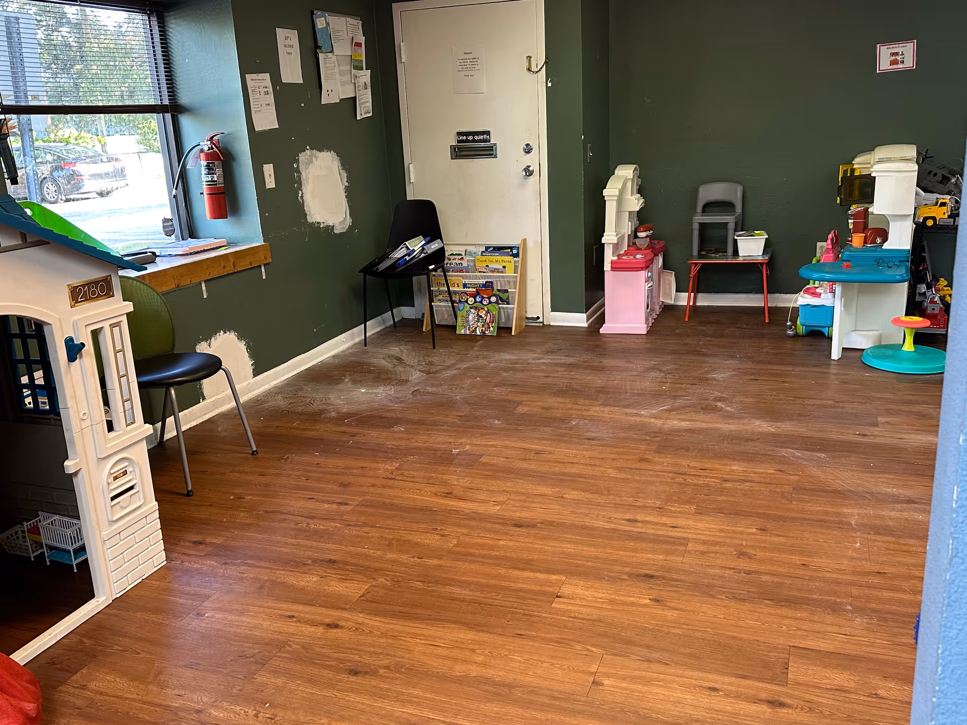Interior room with wooden floor, green walls, window, and children's toy play area.
