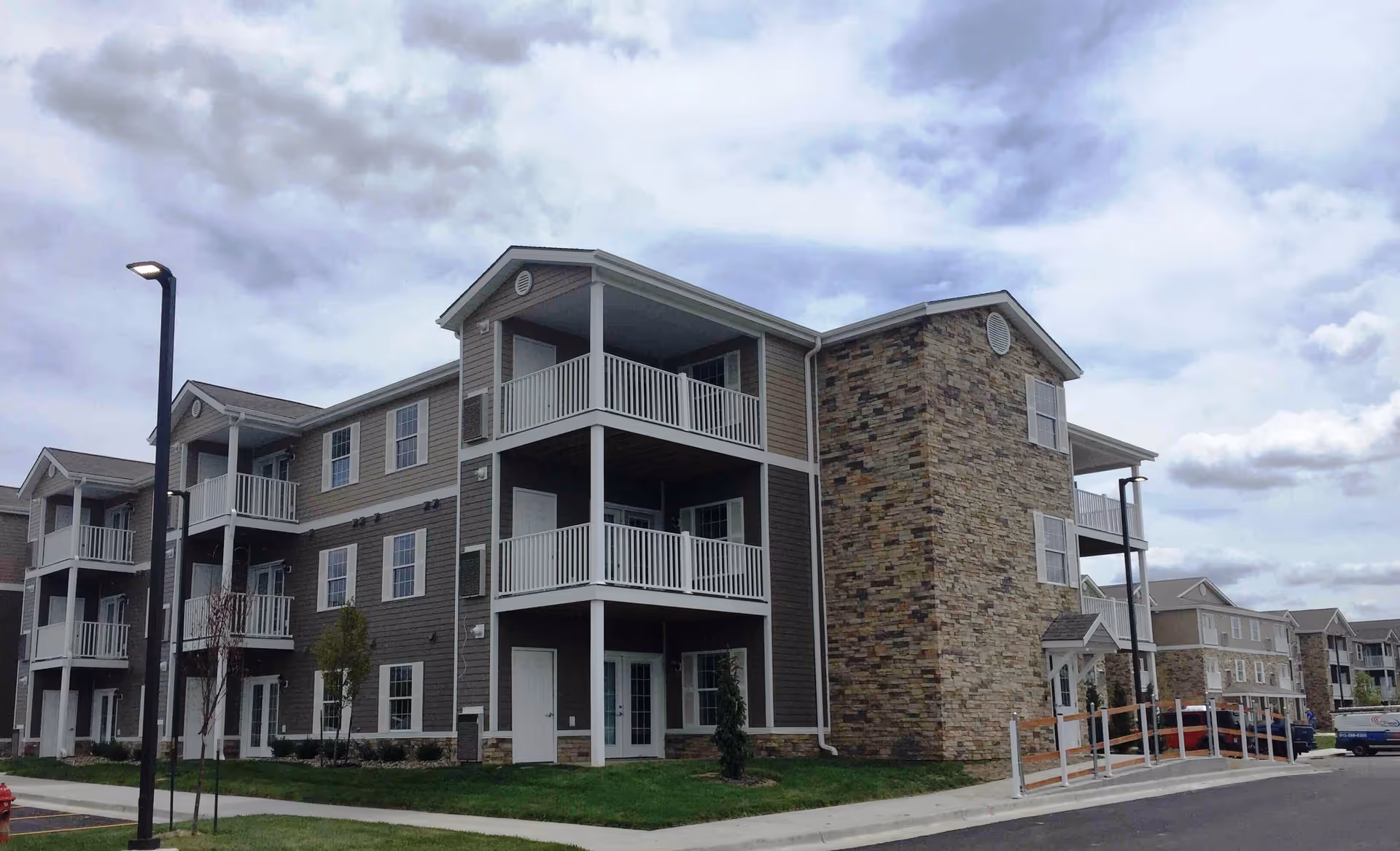 Three-story apartment building with balconies and stone accents under a cloudy sky.