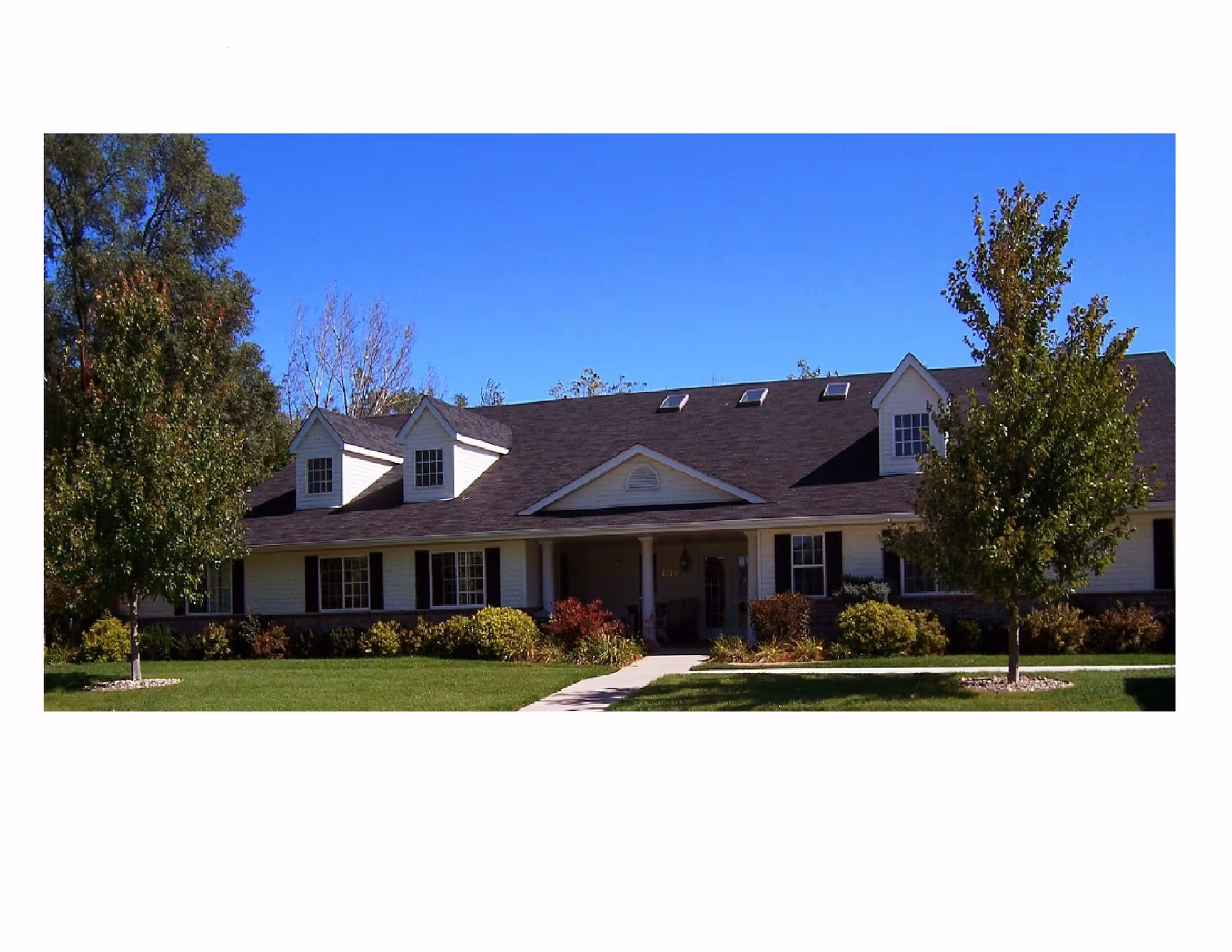 A single-story senior living facility exterior with a front entrance, lawn, and trees.