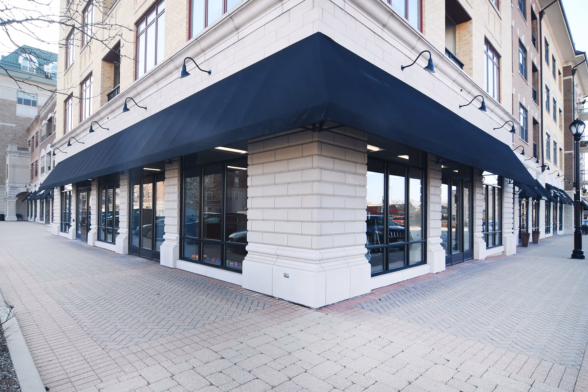 Corner storefront of a brick building with large windows and black awnings.