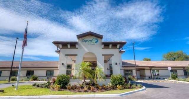 Front view of Inspired Living Tampa facility with palm landscaping and clear blue sky.
